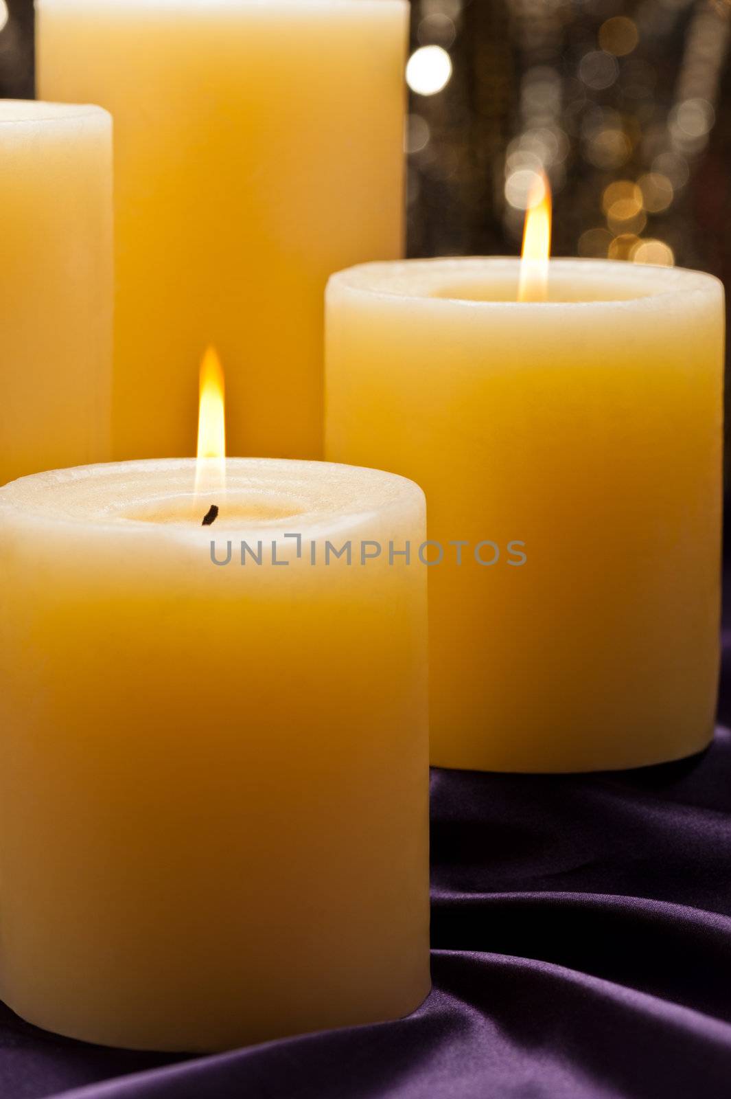 Four candles over purple velvet, with gold glitter background