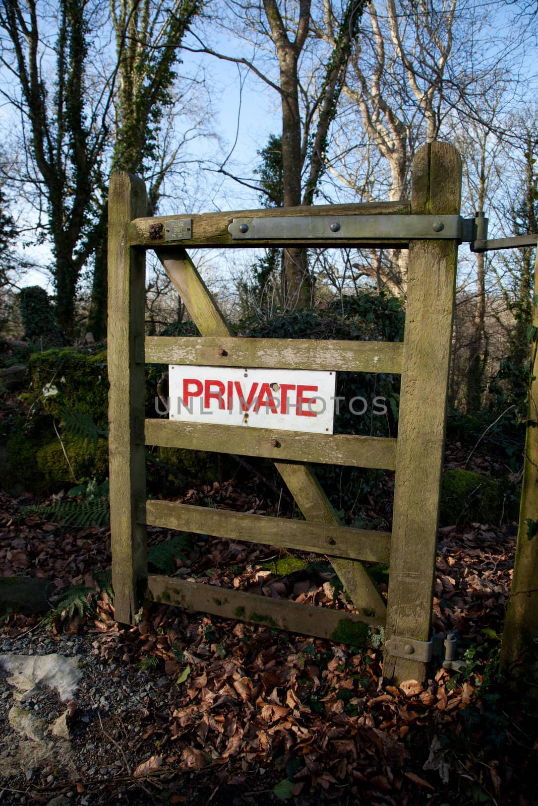 A wooden woodland gate with a white sign with the words 'PRIVATE' in red.