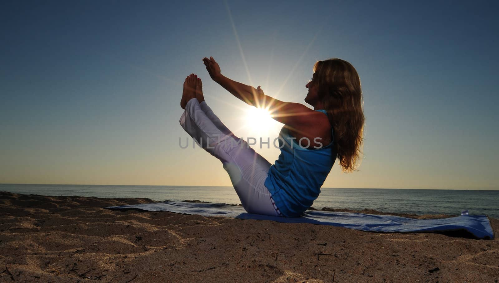 Woman doing full boat yoga pose on beach with sunrise
