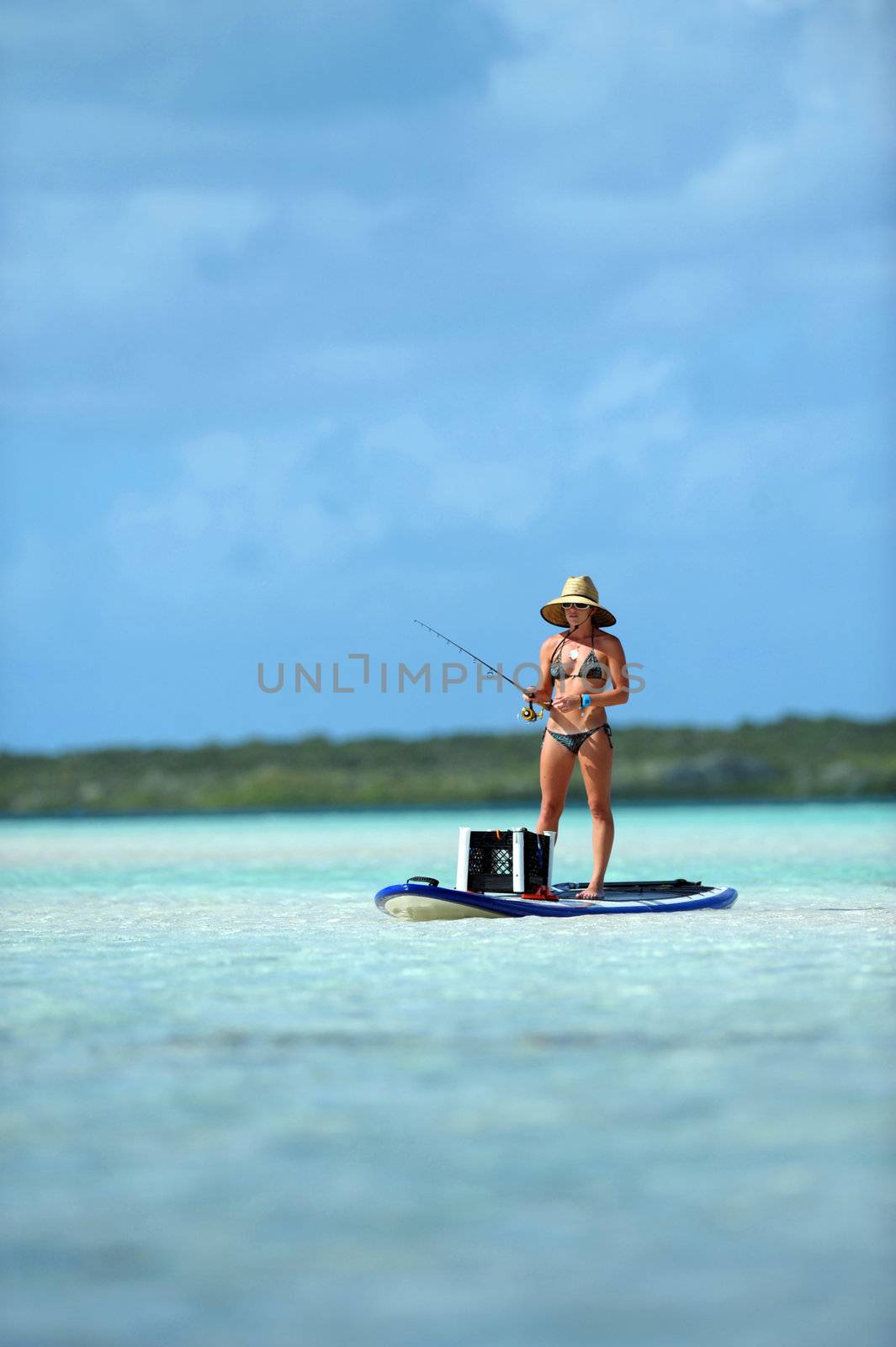 Beautiful woman in bikini fishing in scenic tropical destination from paddleboard