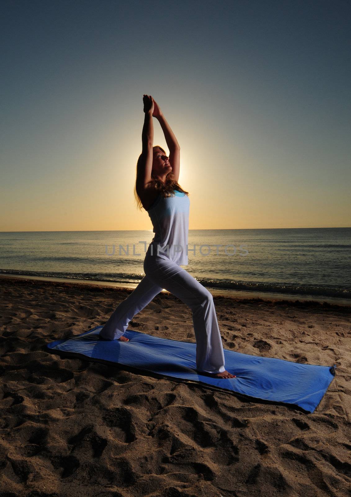 Woman doing Warrior Pose I (Virabhadrasana I) yoga pose on beach during a beautiful sunrise