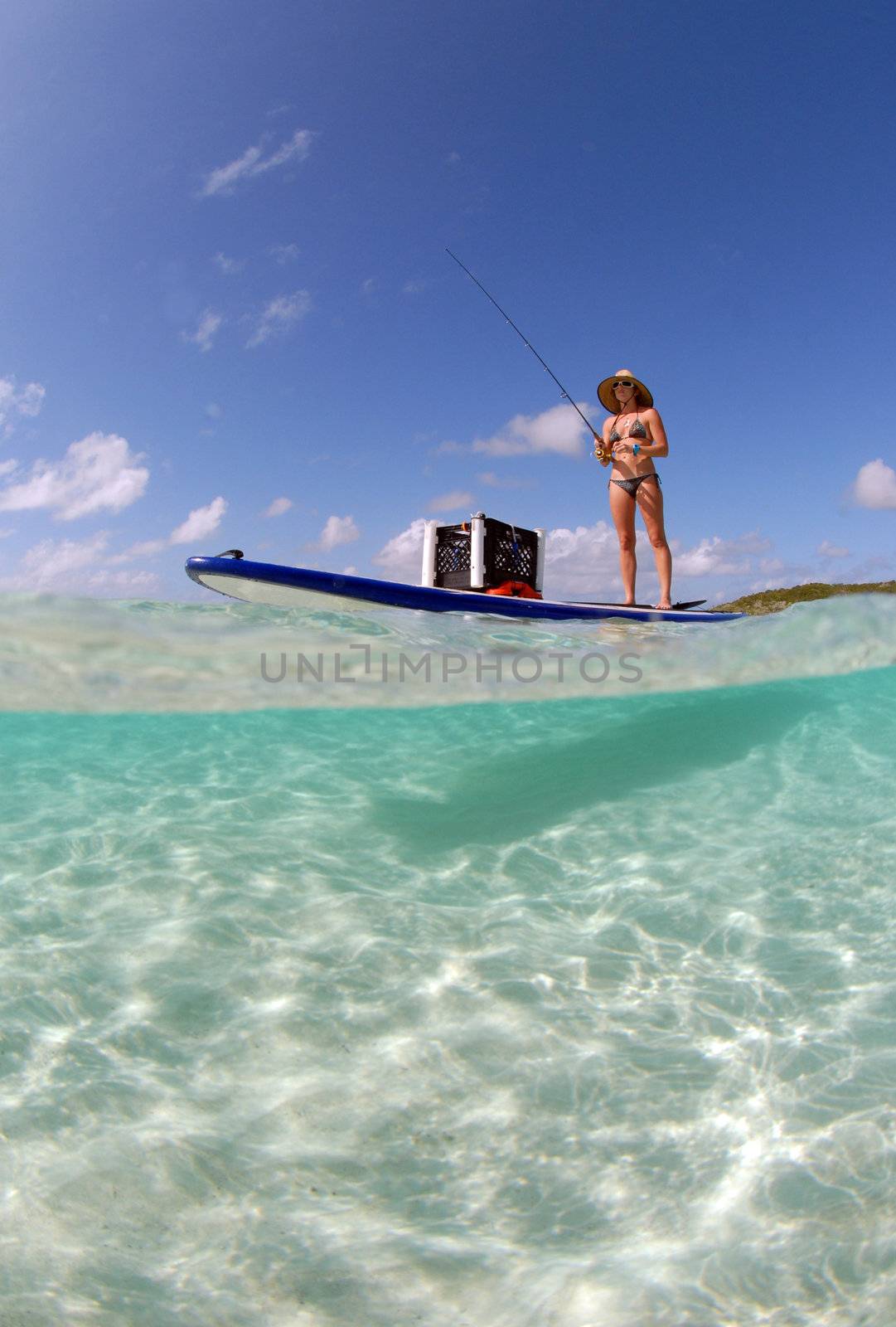 Beautiful woman in bikini fishing from paddle board in tropical destination