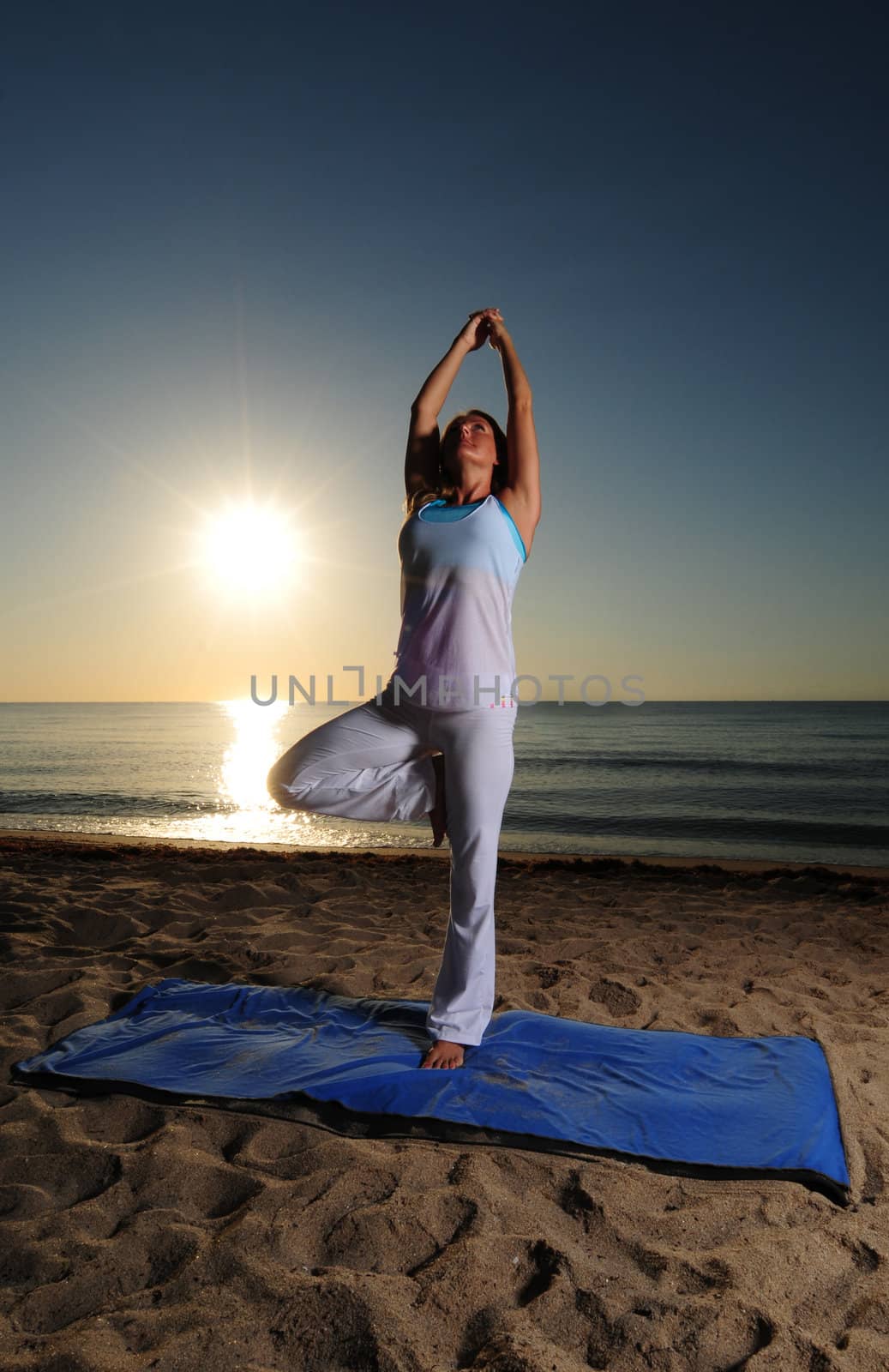 Woman doing tree yoga pose on beach during a beautiful sunrise