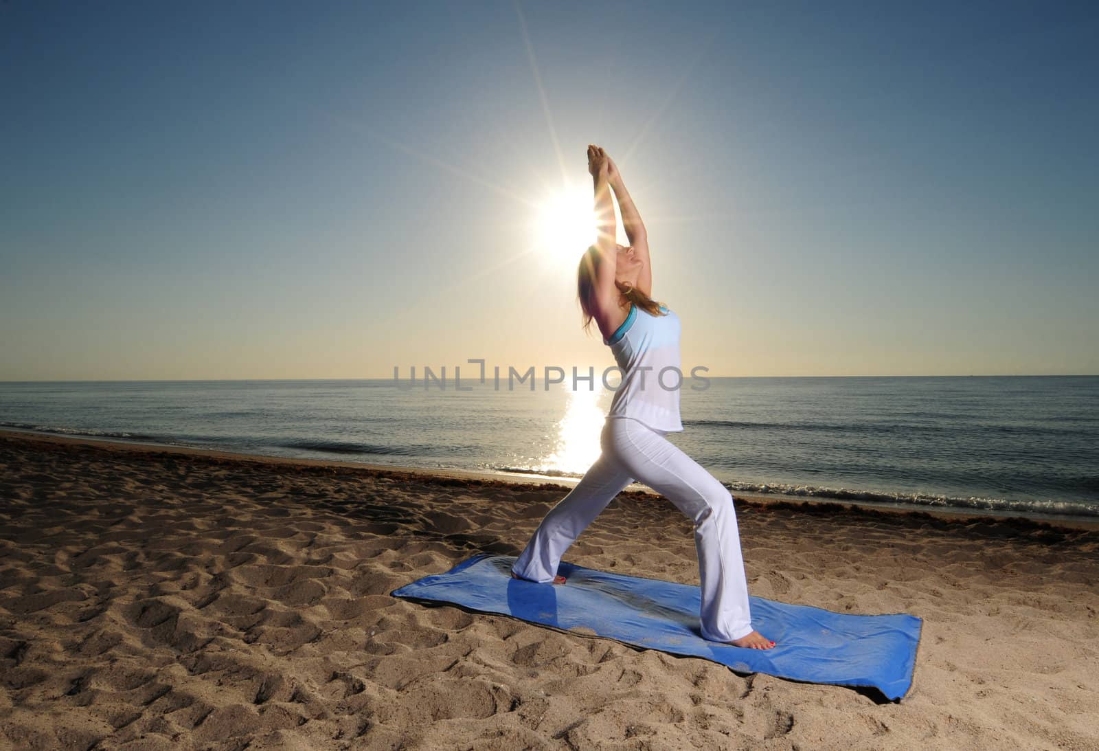 Woman doing yoga pose on beach with sunburst