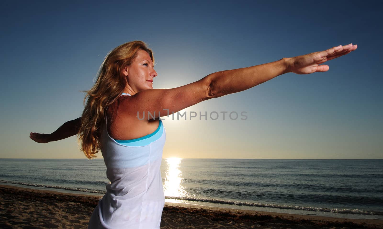 Woman doing Warrior Pose II (Virabhadrasana II) yoga pose on beach during a beautiful sunrise