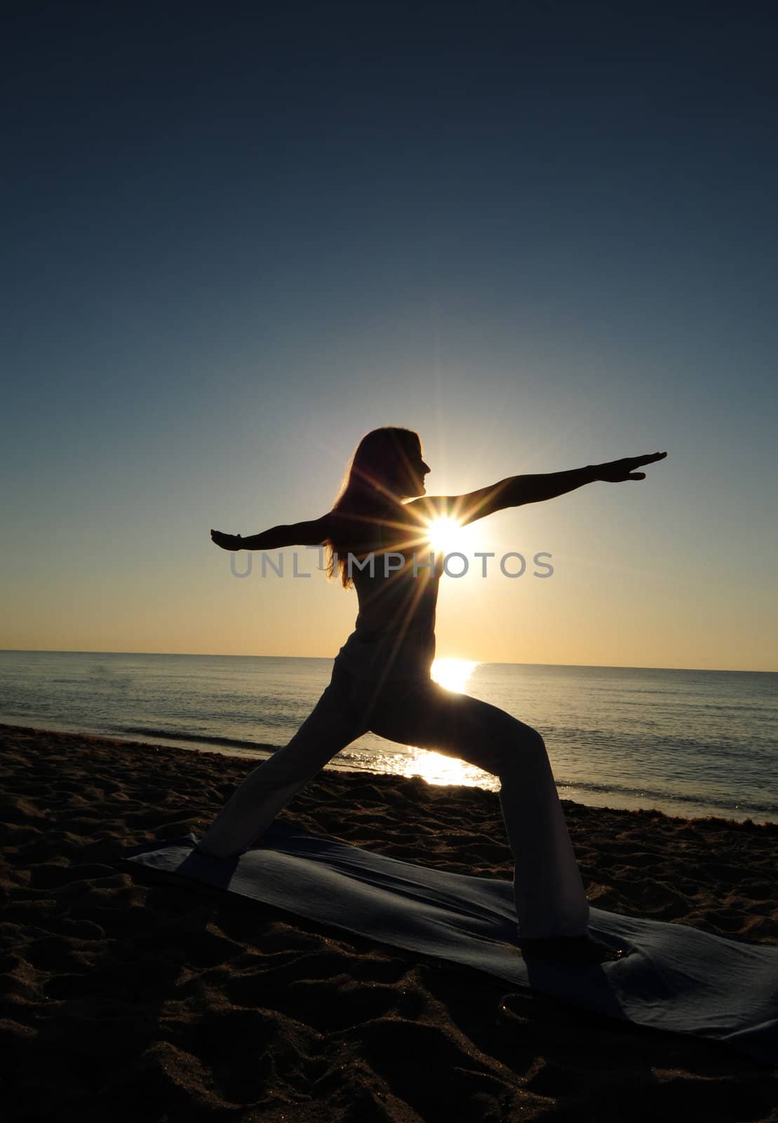 Woman doing Warrior II yoga pose on beach during a beautiful sunrise