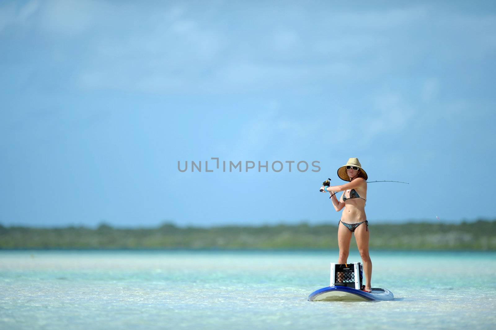 Beautiful woman casting fishing rod while paddleboarding in the Caribbean