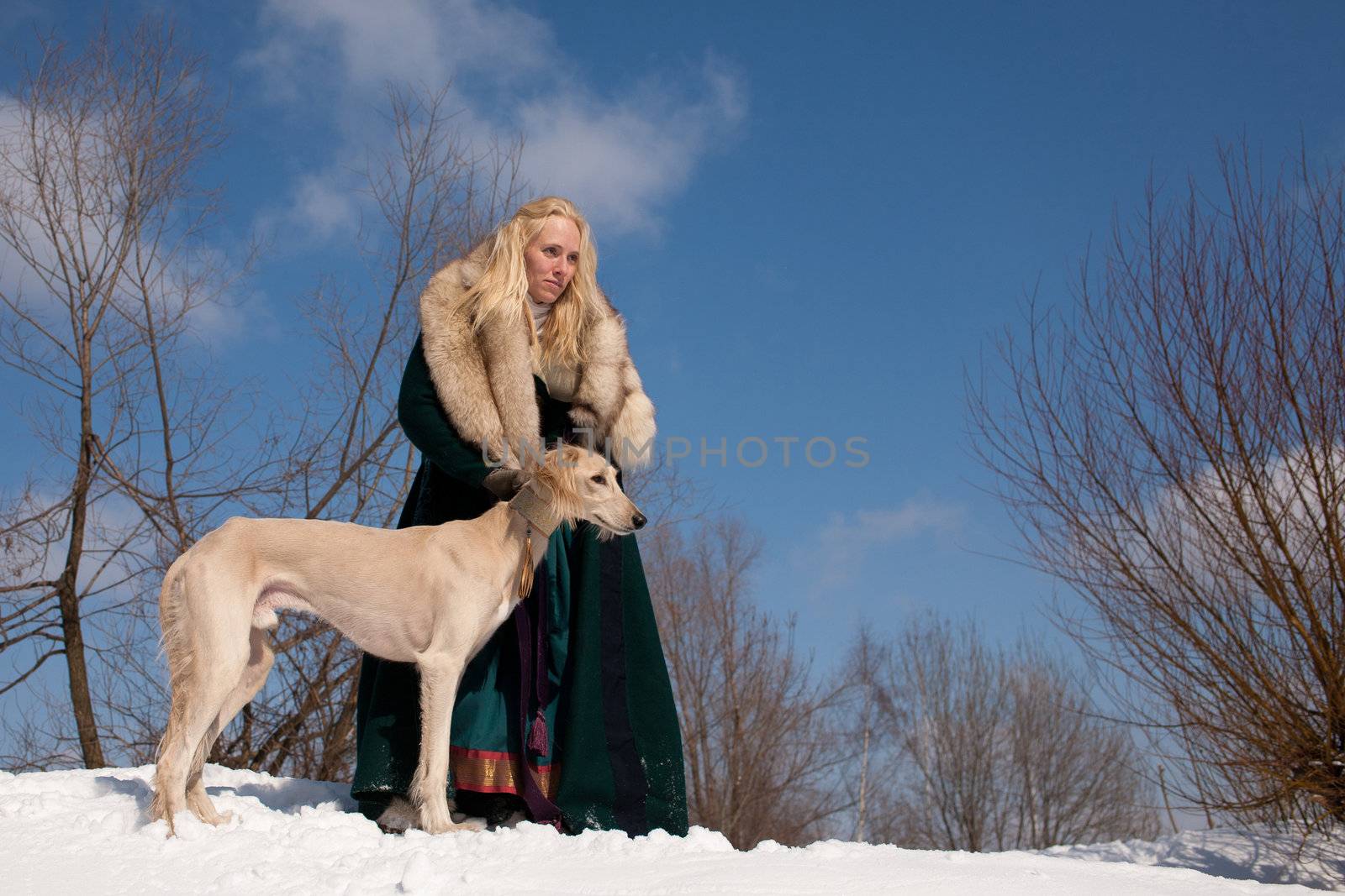 A blonde girl and a standing white saluki on snow
