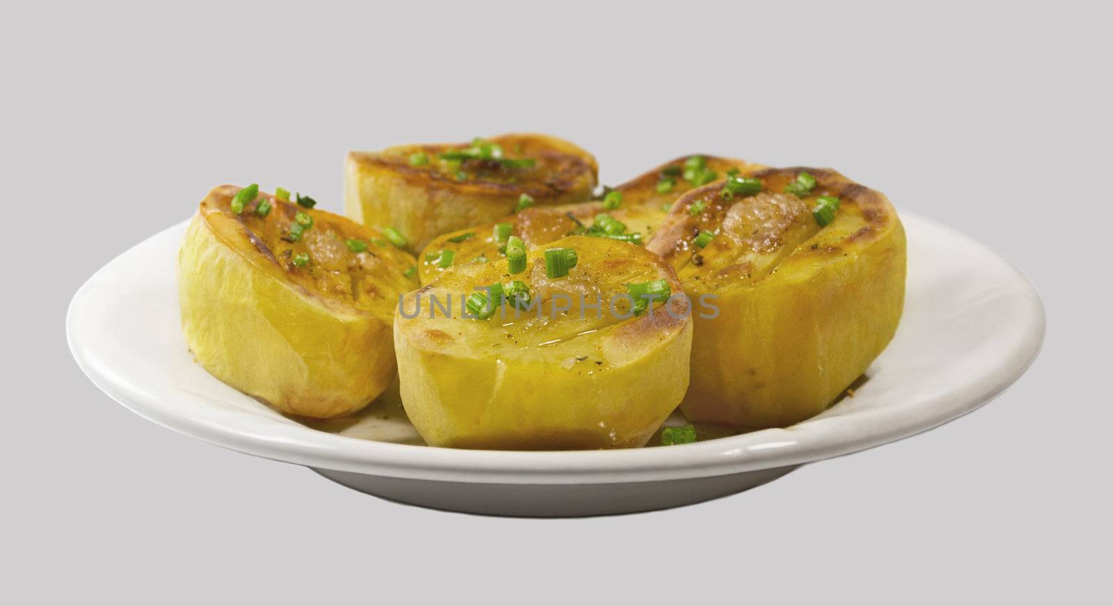 Baked potato with golden crust on white plate. Isolated on a light gray background.