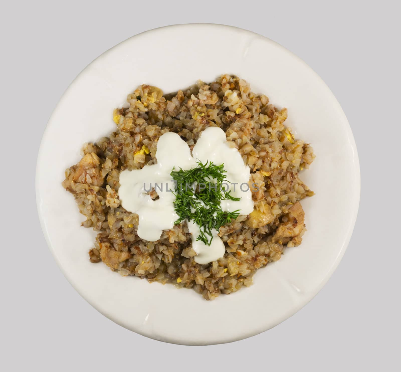 Buckwheat porridge, mixed with grated egg and poured sour cream with dill on white plate. Isolated on a light gray background.