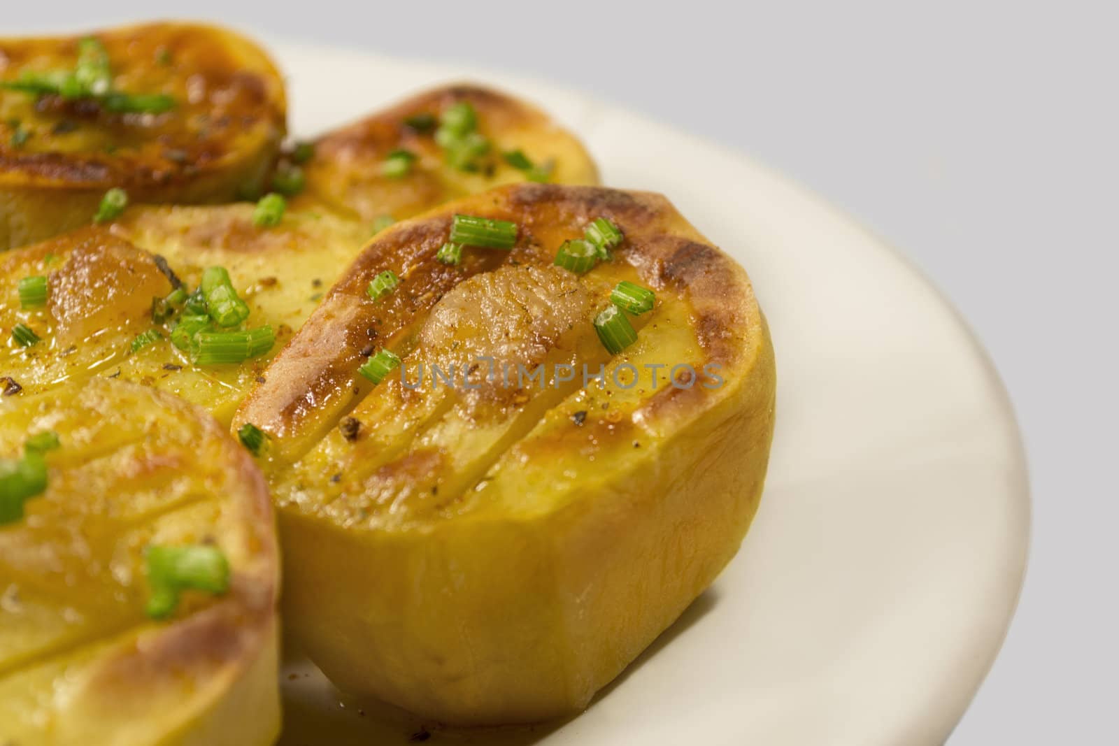 Baked potato with golden crust on white plate. Isolated on a light gray background.