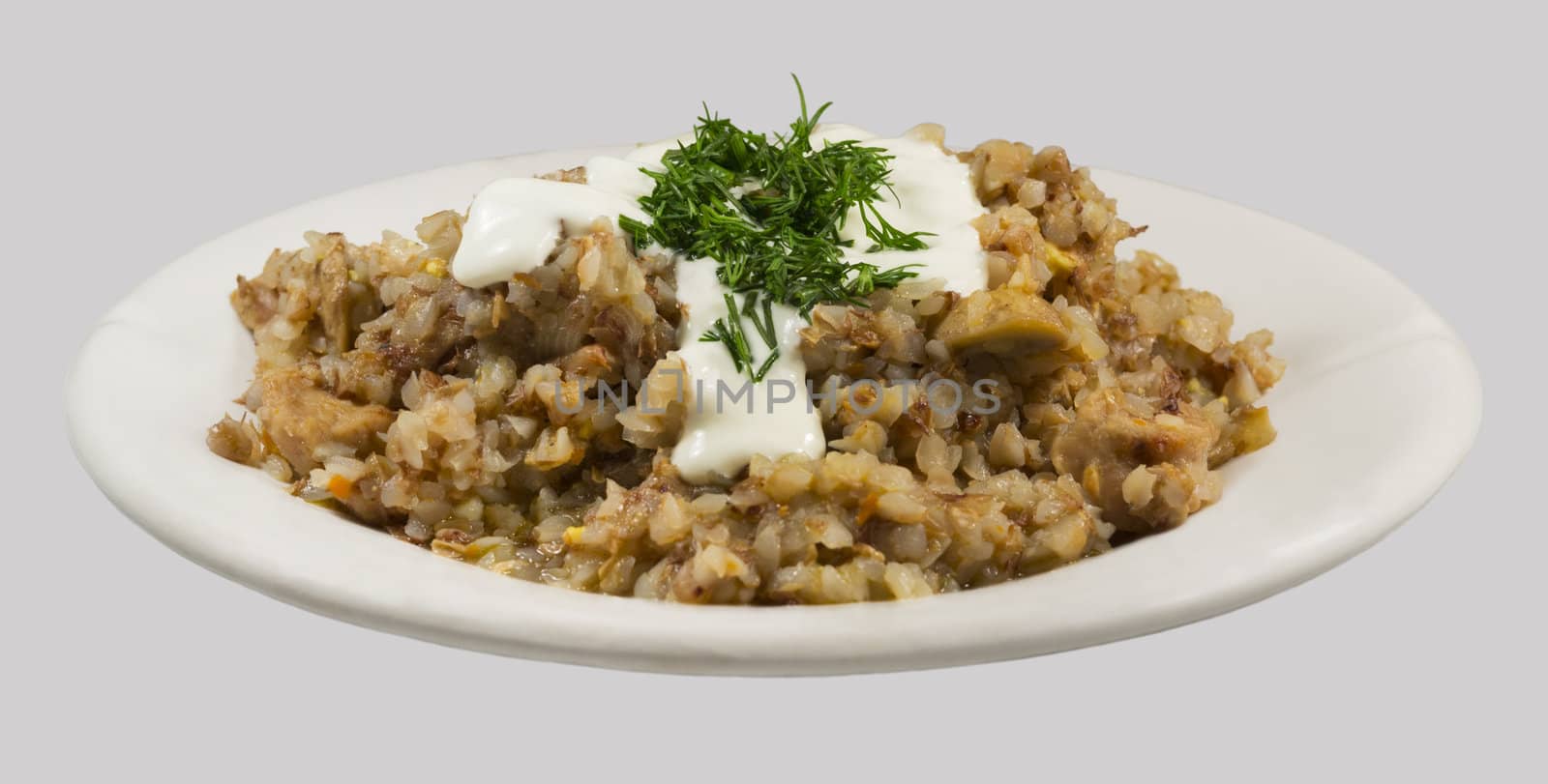 Buckwheat porridge, mixed with grated egg and poured sour cream with dill on white plate. Isolated on a light gray background.