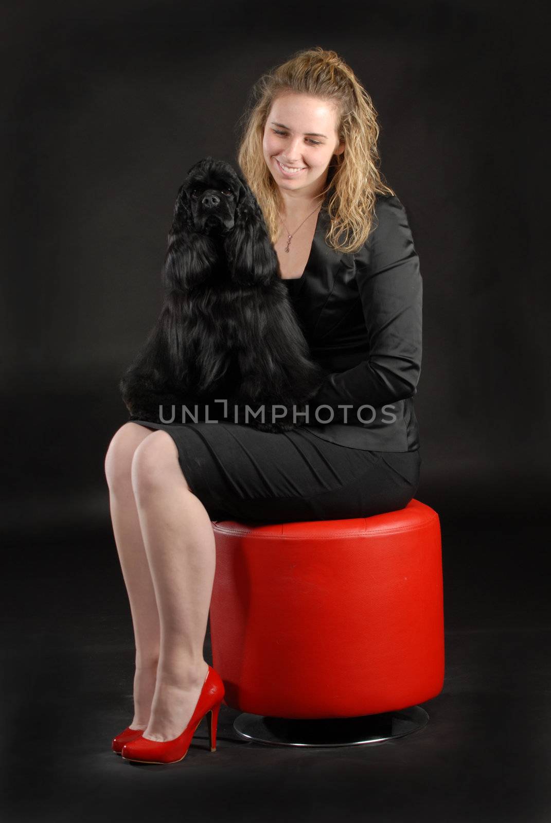 woman and dog - american cocker spaniel sitting on lap of lady wearing black dress sitting on red stool