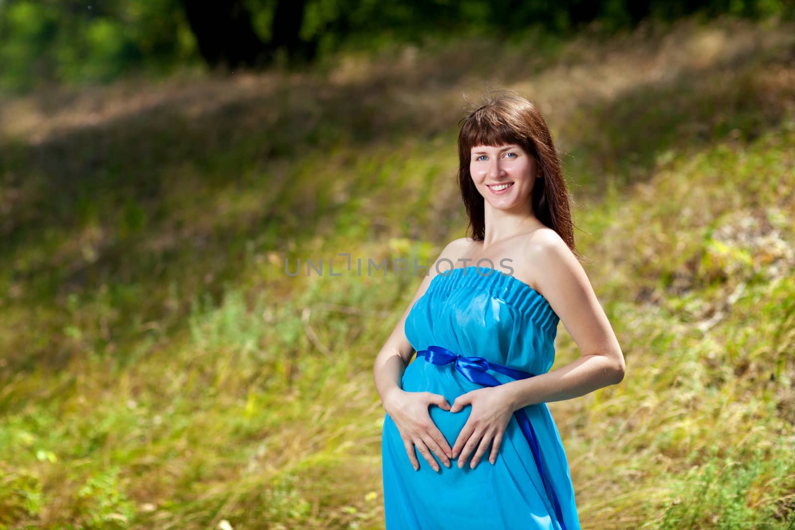 happy girl made heart with hands on the pregnant belly