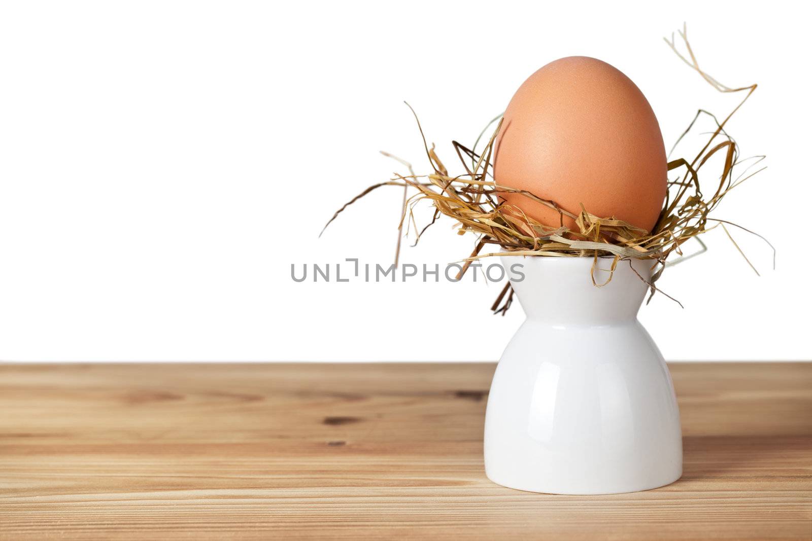 Easter egg in hay nest on white stand. Natural egg. All on old wooden table on white background, isolated

