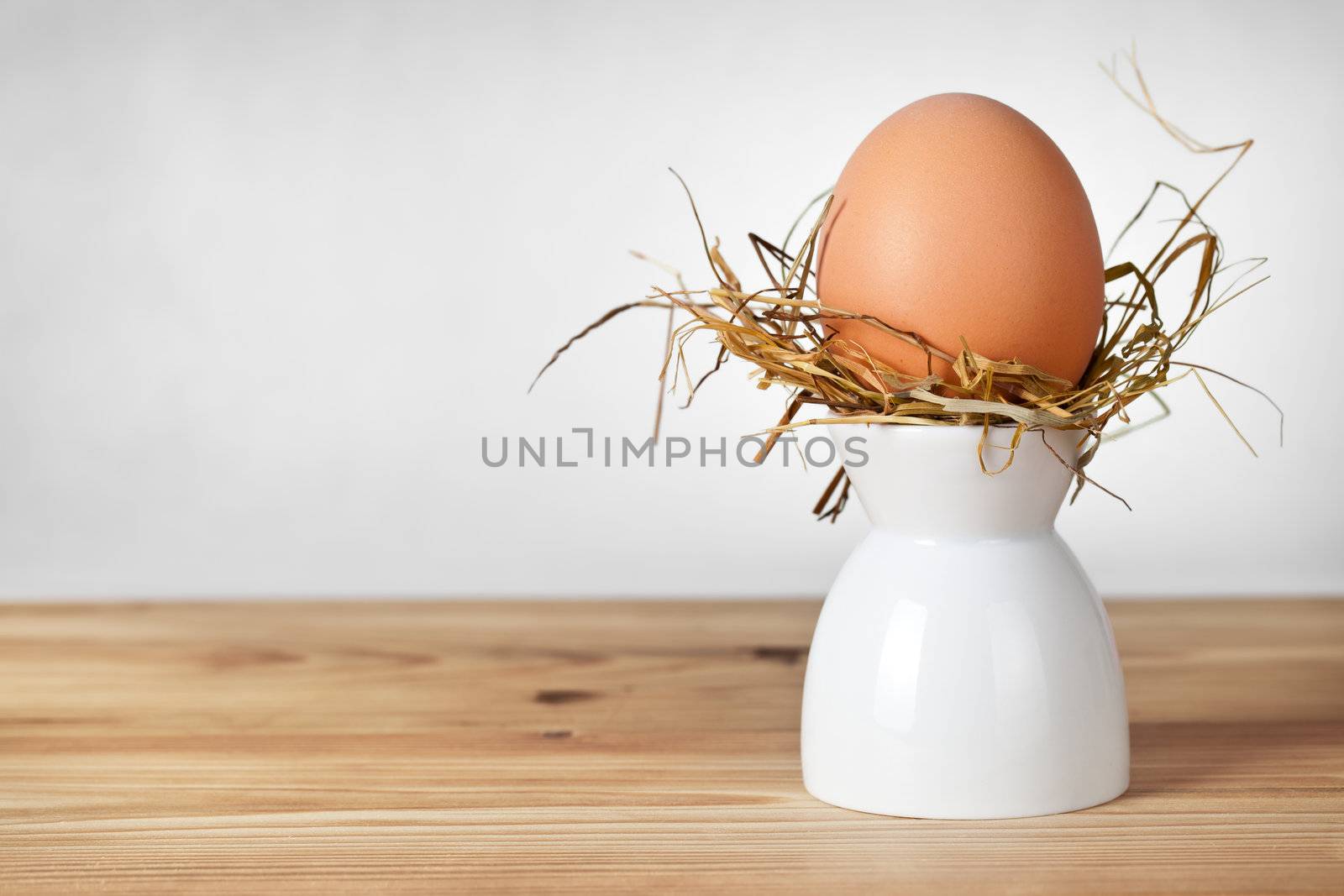 Easter egg in hay nest on white stand. Natural egg. All on old wooden table background