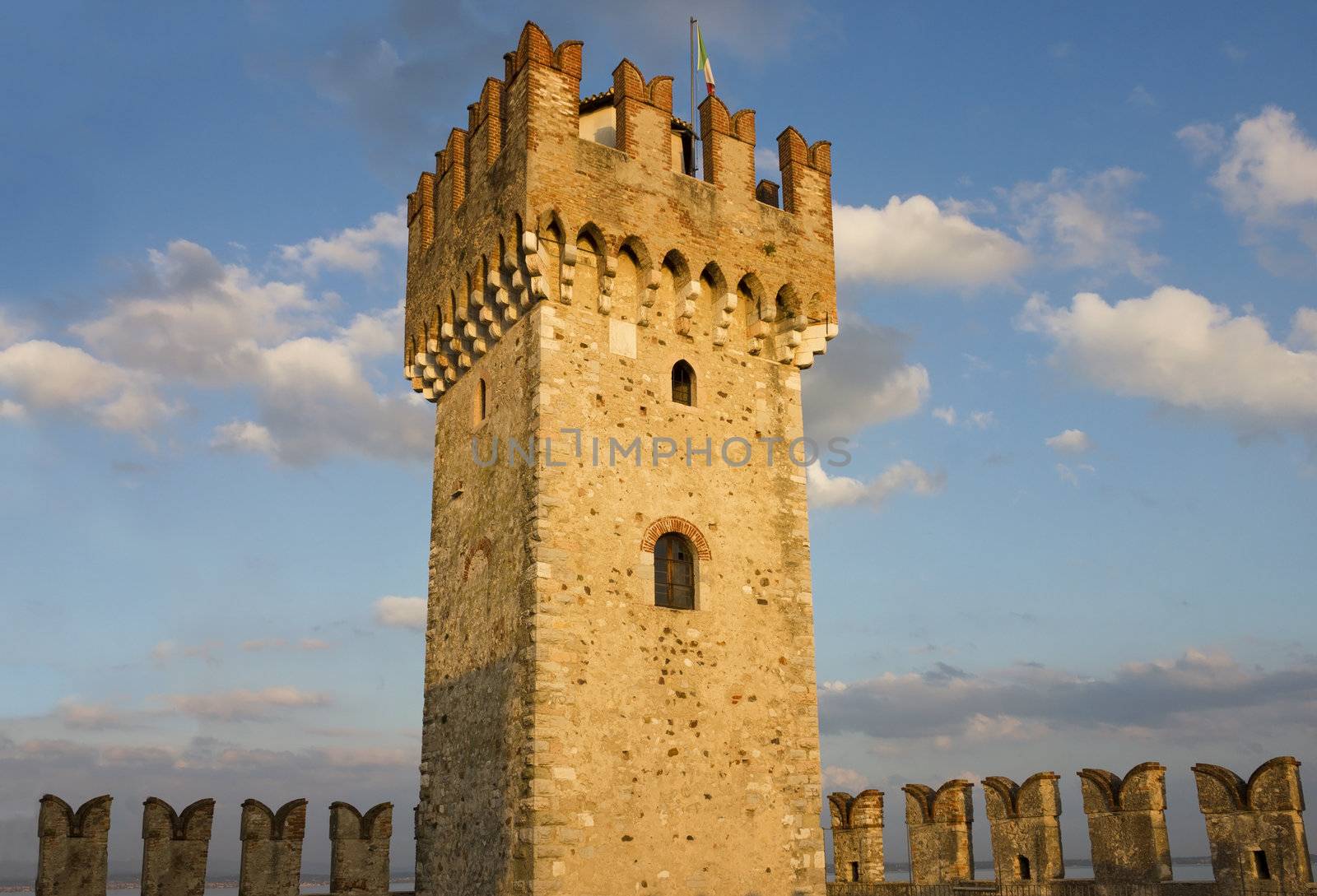 Close up shot of the Tower of Scaliger Fortress in Sirmione, Italy in the warm light of the sunset with colorful clouds over the blue sky. 