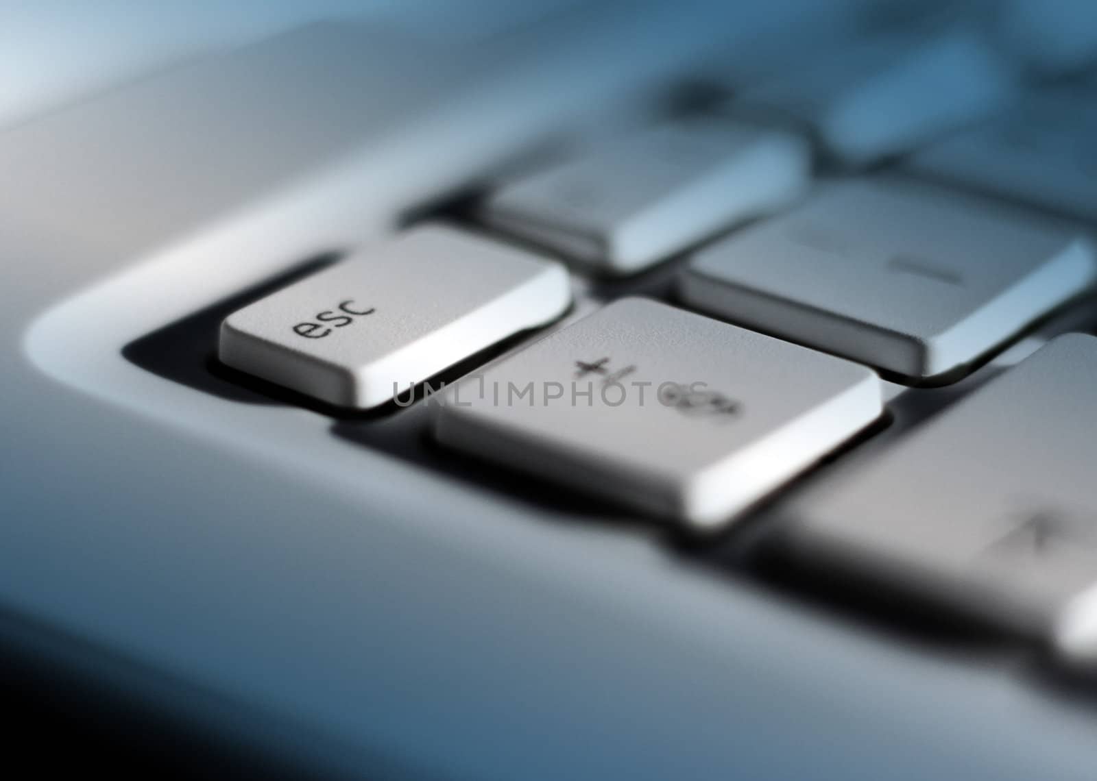 Close-up of laptop keyboard with focus on escape key. Blue lighting effect added with clear patch on escape key.
