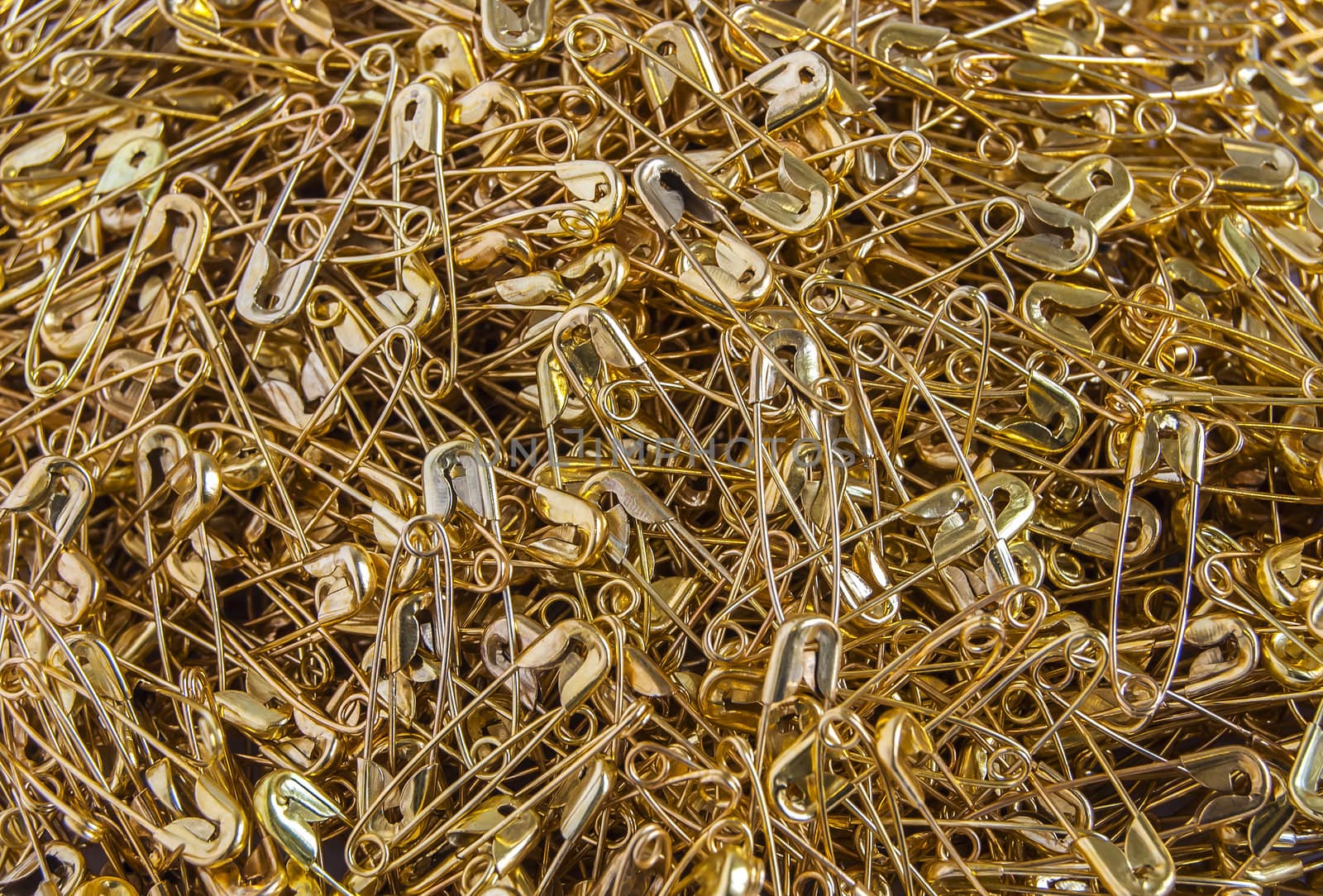 Gold colored safety pins pile closeup as background