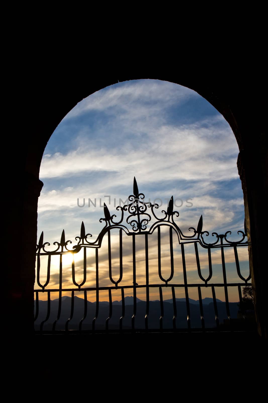 The sun sets over the Spanish mountains through an old stone arch in Ronda.