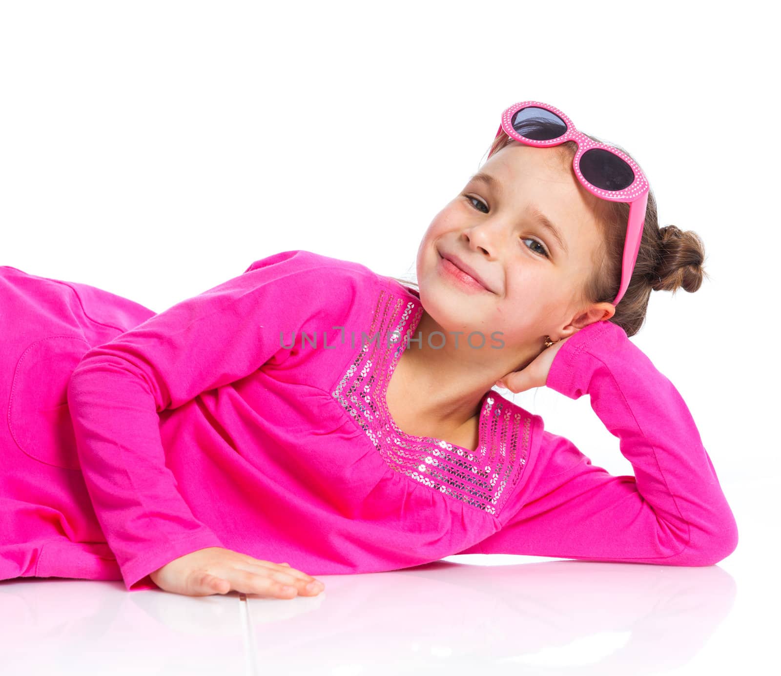 Little fashion girl lying in pink dress and sunglasses. Isolated white backround.