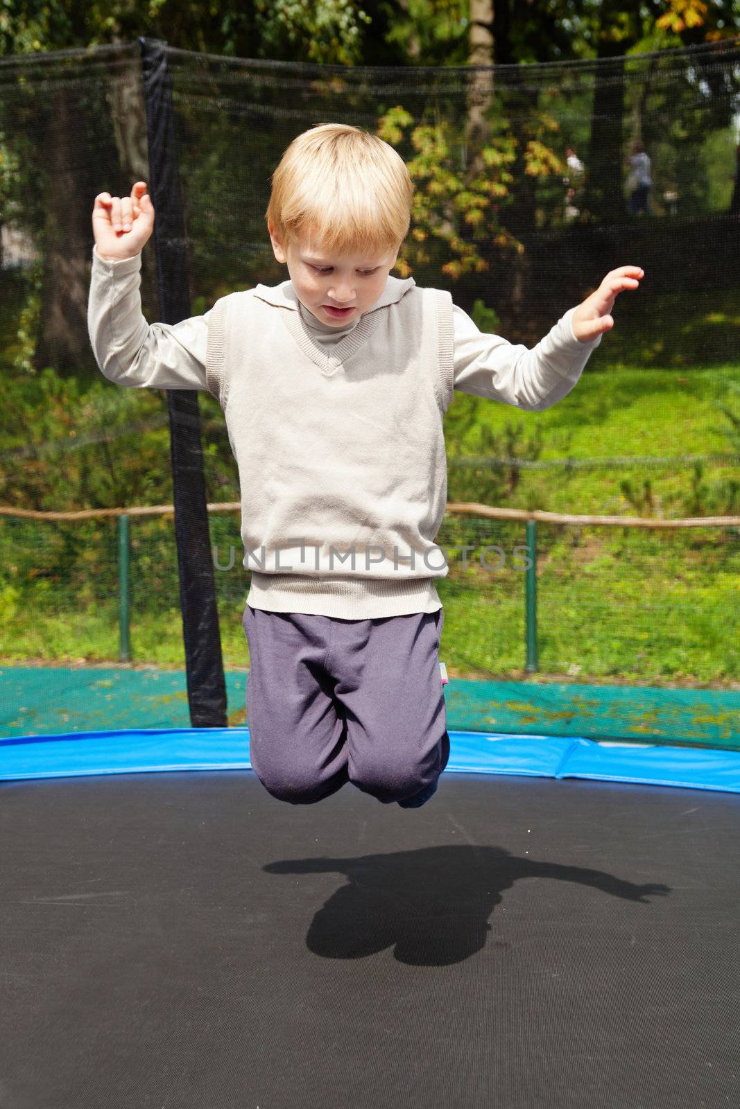 Blond boy jumping on trampolin at an outdoor playground