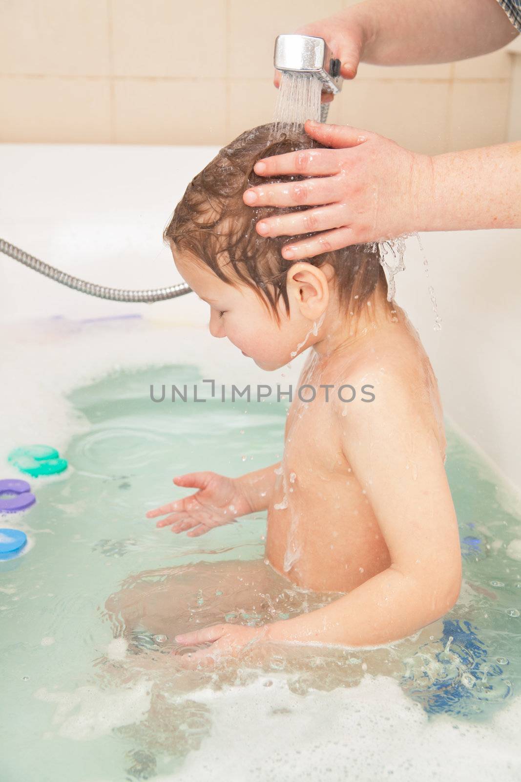 Little boy taking bath, hands of his mother washing his head