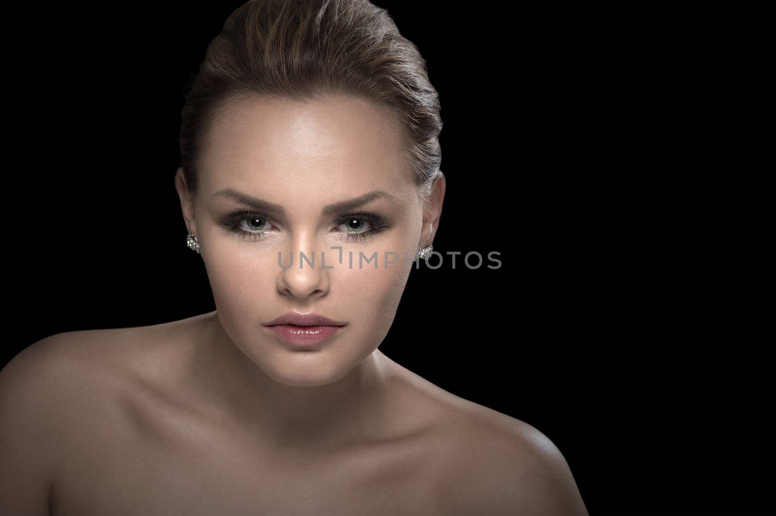 Studio portrait of a beautiful serious intense young woman with bare shoulders looking directly at the camera against a dark background with copy space