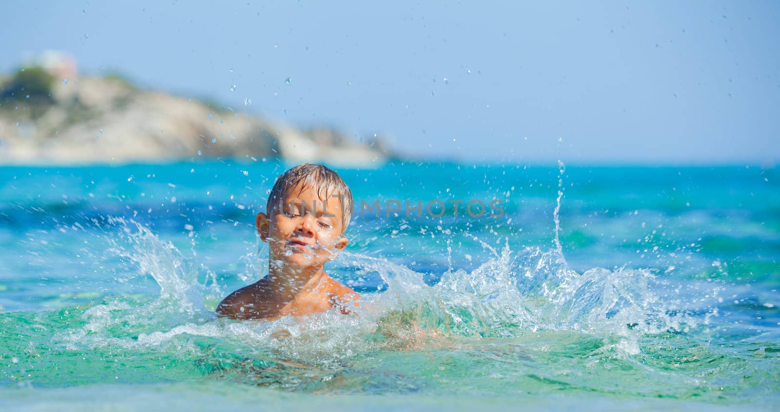 Portrait of young boy swimming and squirting in the transparent sea