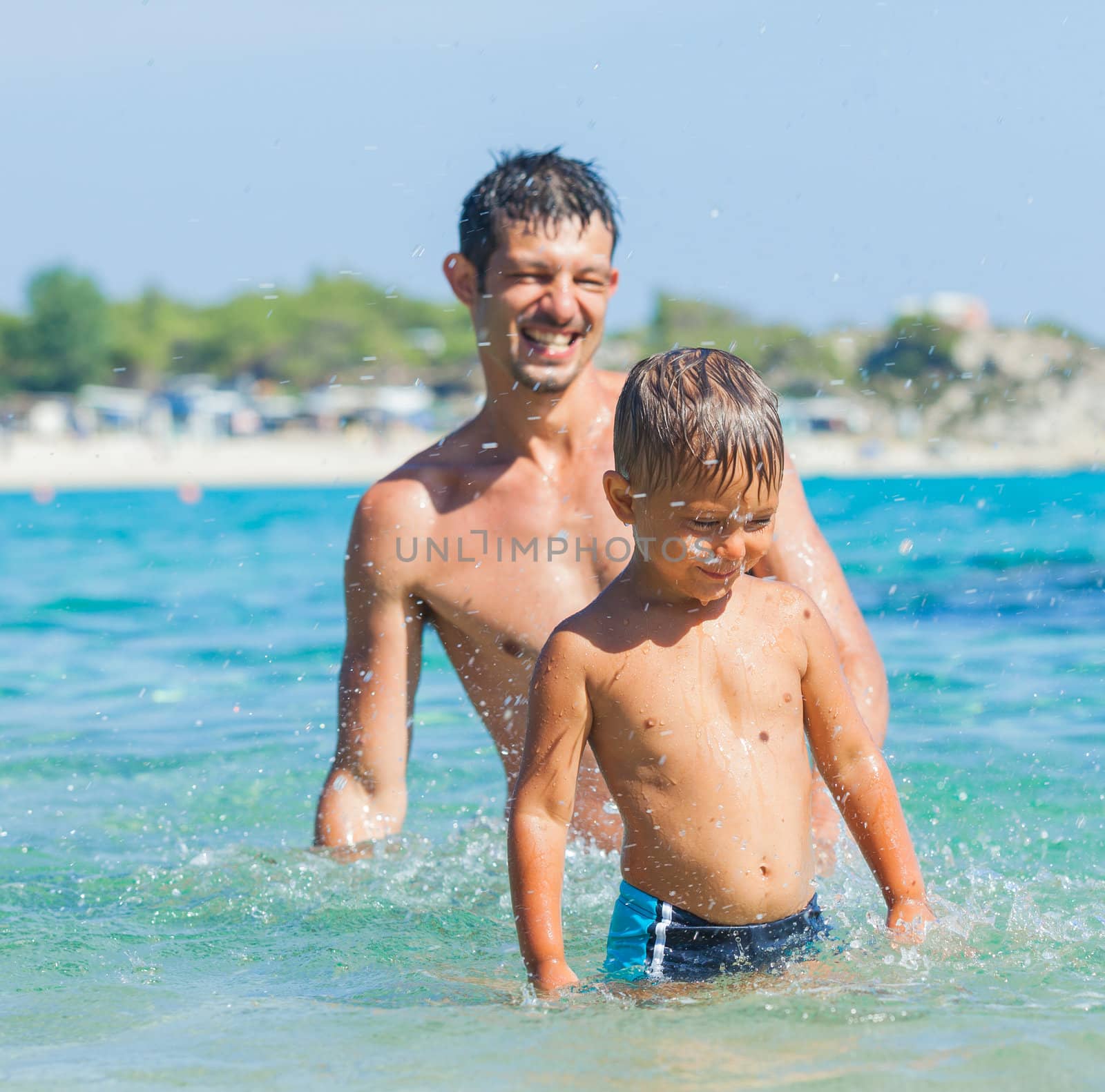 Portrait of cute boy plaing with his father in the transparent sea