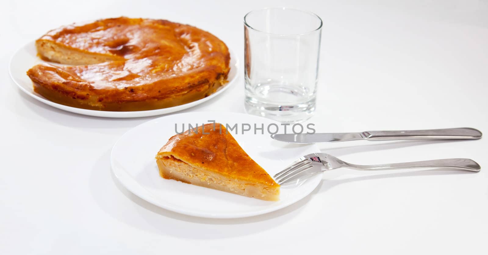Piece of onion pie with fork and knife and glass on white background