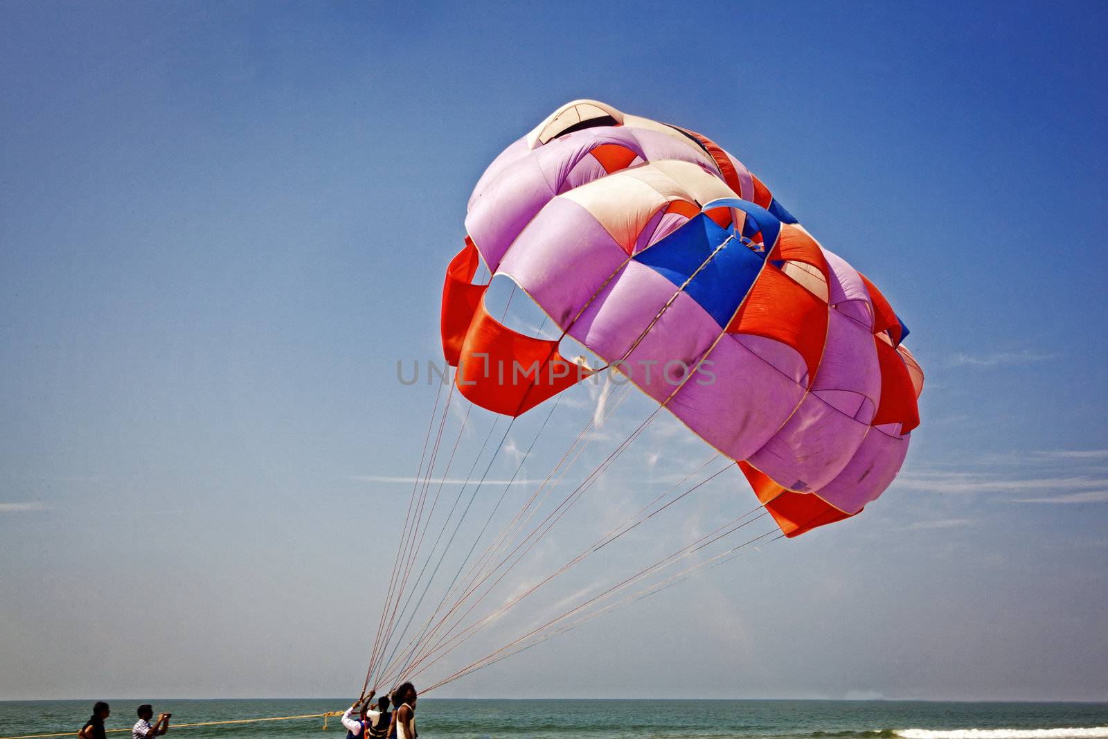 Landscape of paraglider taking off with the parachute leaving a trail of sand blowing in the breeze watched by roadies and friend, location of shot Goa, India