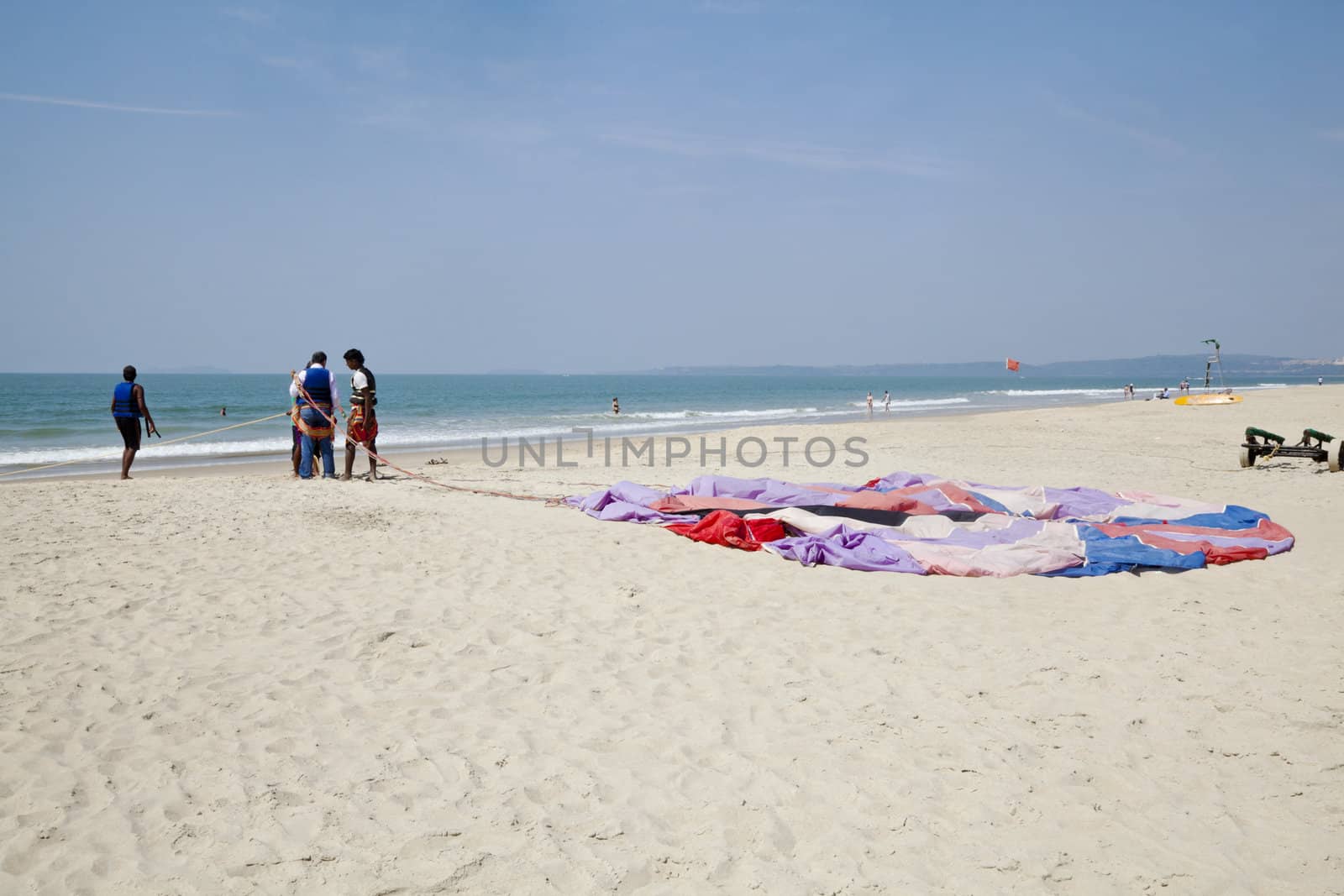 Workers getting a customer ready for paragliding over the sandy shoreline on a secluded beach patrolled by lifeguards