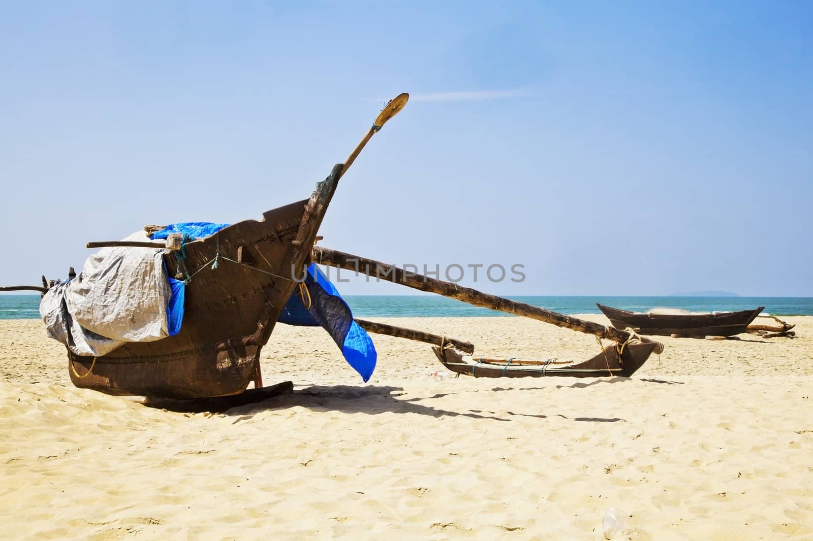 Horizontal landscape of a pair of fishermans fishing catamarans moored on the sandy beach containning his tackle and nets covered by tarpaulins at Goa, India