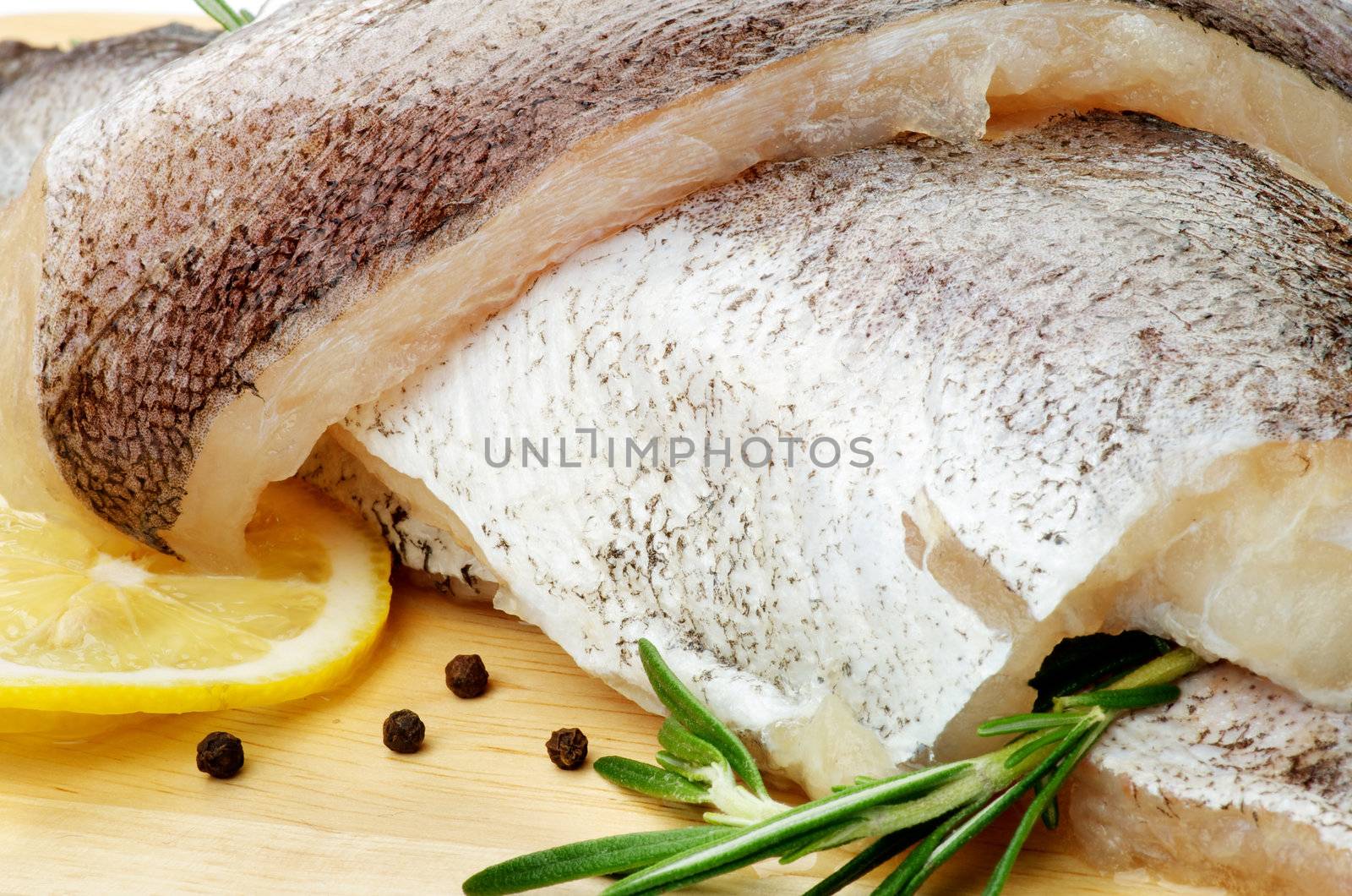Fillets of Raw Fish Hake with Lemon, Black Peppercorn and Rosemary closeup on Cutting Board