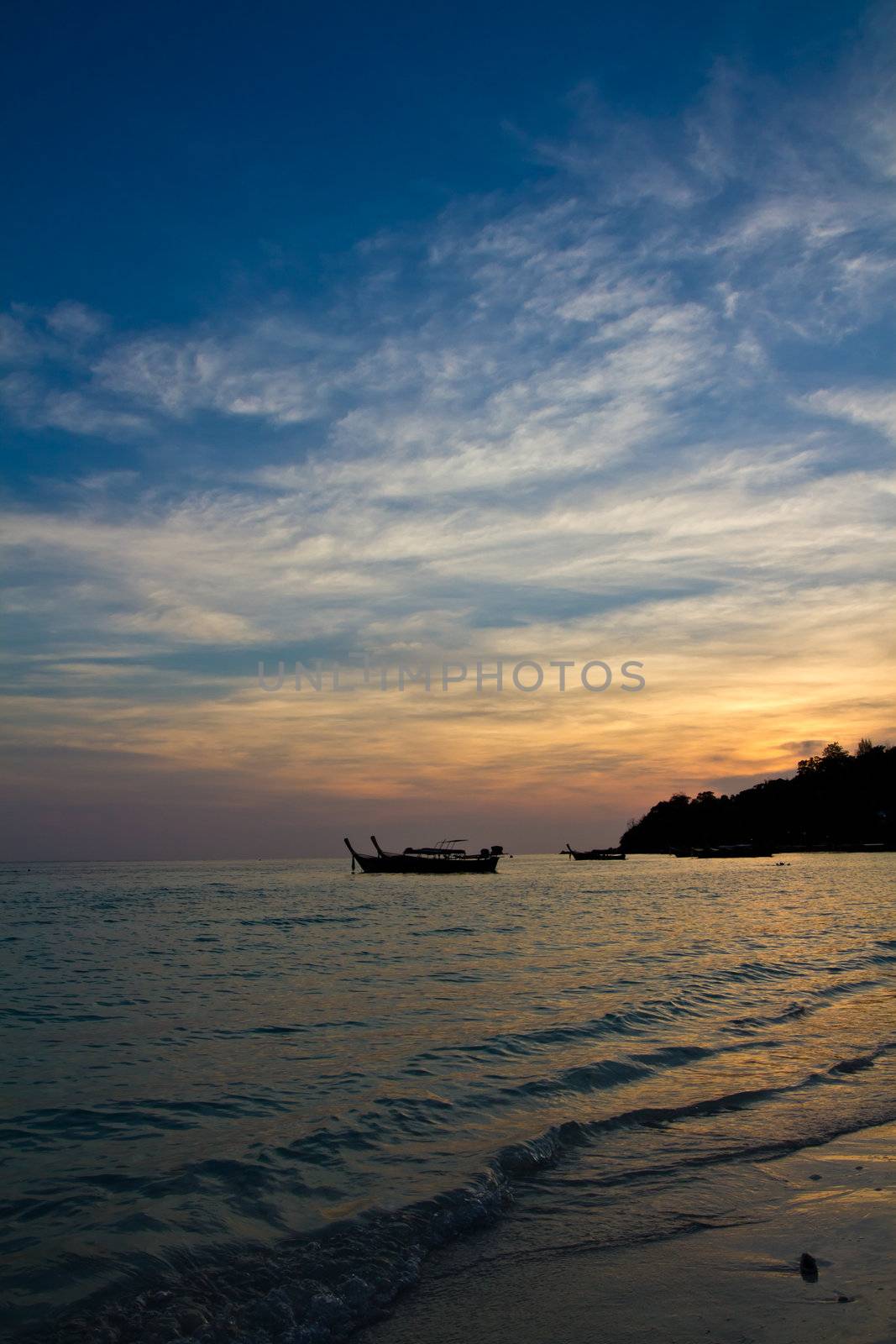 The sun goes down over longtail boats on a beach in Thailand.