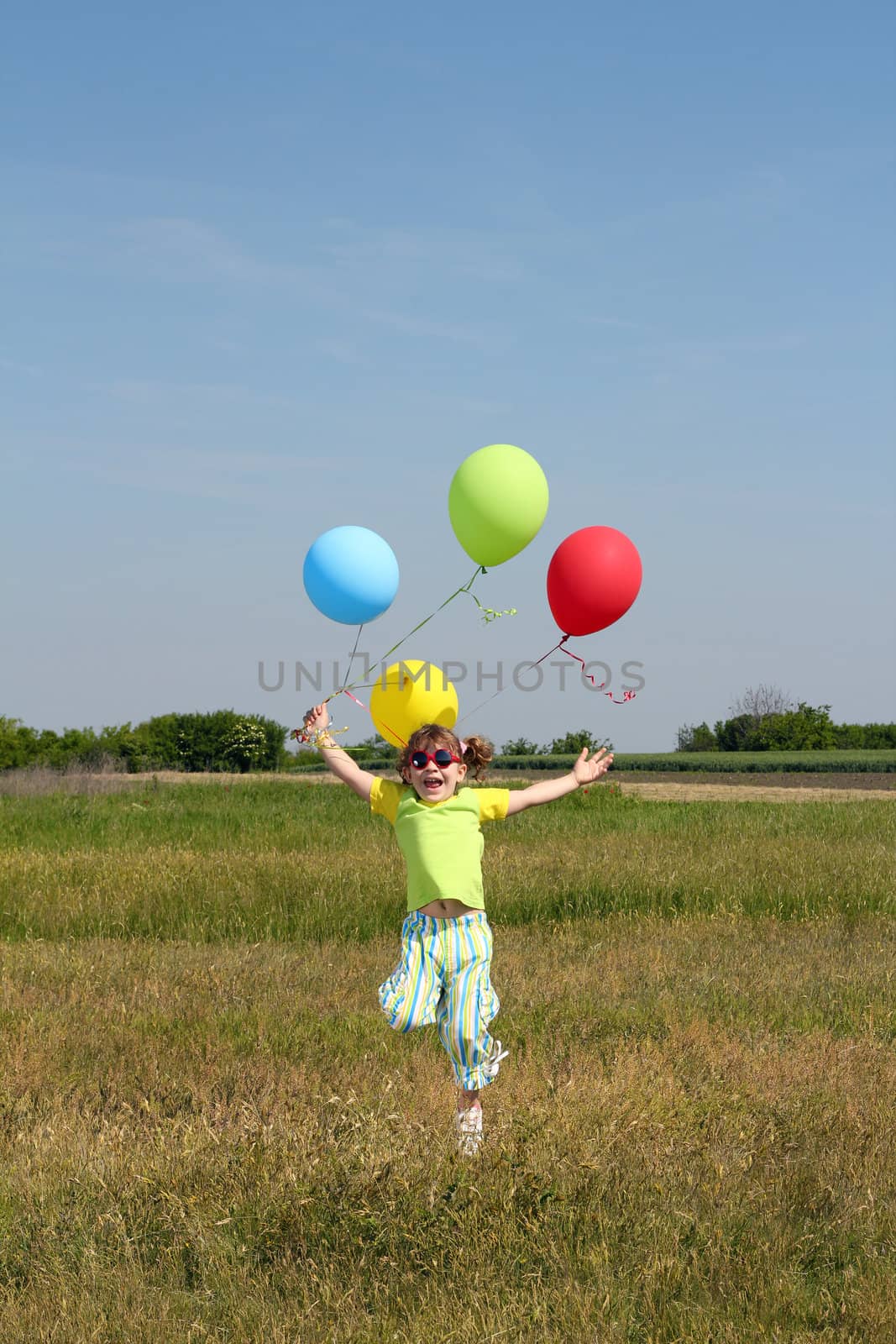 happy little girl with balloons jumping on field by goce