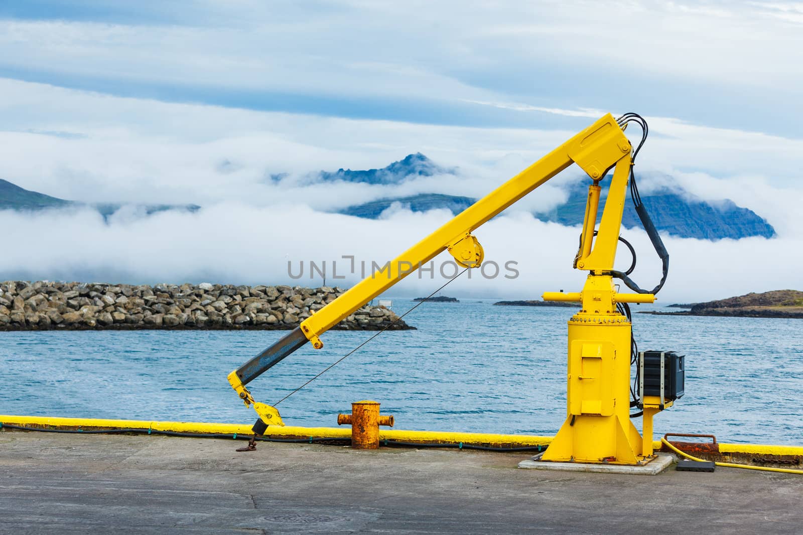 Fishing crane in small seaside Iceland town harbor. Clouds in Mountains