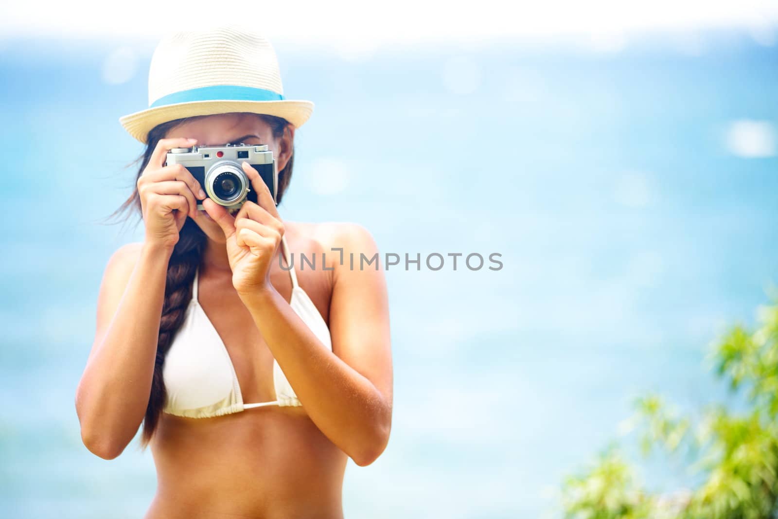 Summer beach woman holding vintage retro camera taking pictures looking at camera during summer holiday vacation travel at the ocean.