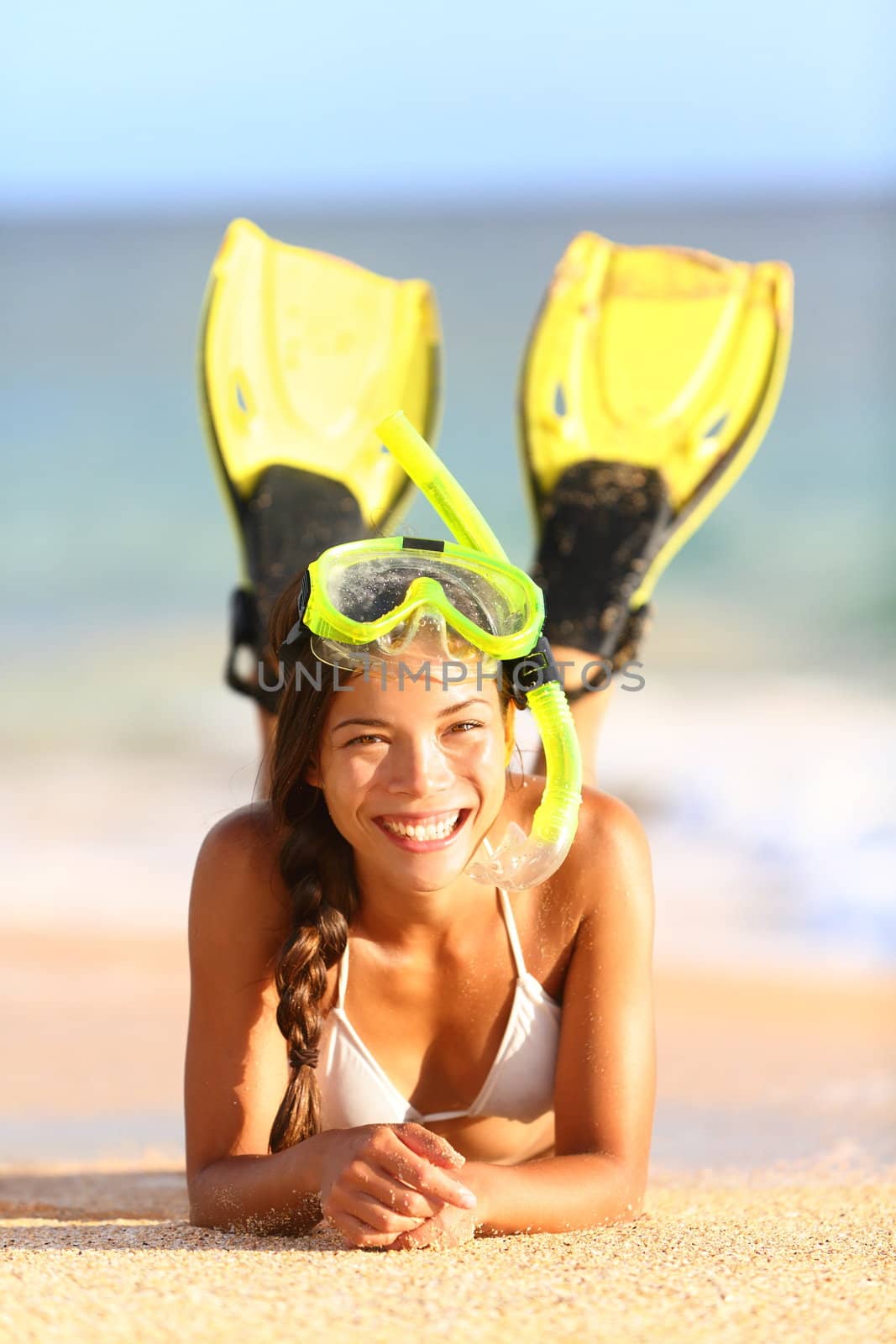 Beach holiday vacation woman snorkeling fun. Joyful happy woman wearing snorkeling equipment, fins and mask, lying down in water and sand looking at camera. Beautiful mixed race Caucasian / Asian bikini model.