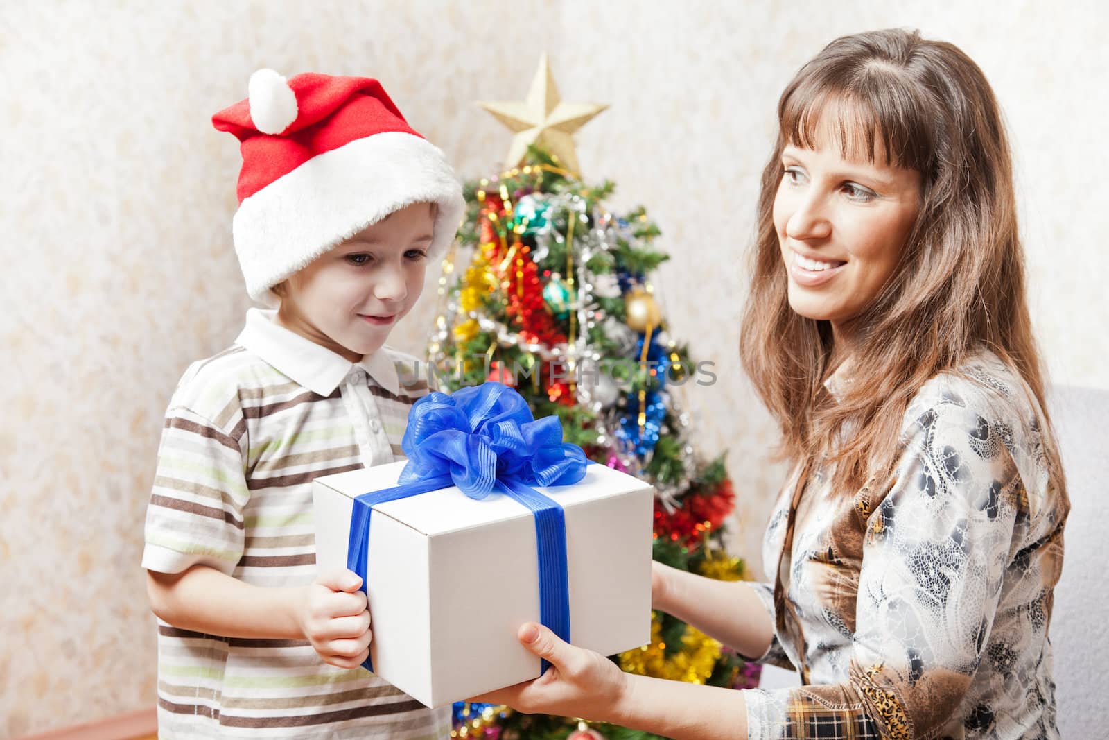 Smiling mother giving new year present or christmas holiday gift box to little son wearing Santa Claus hat