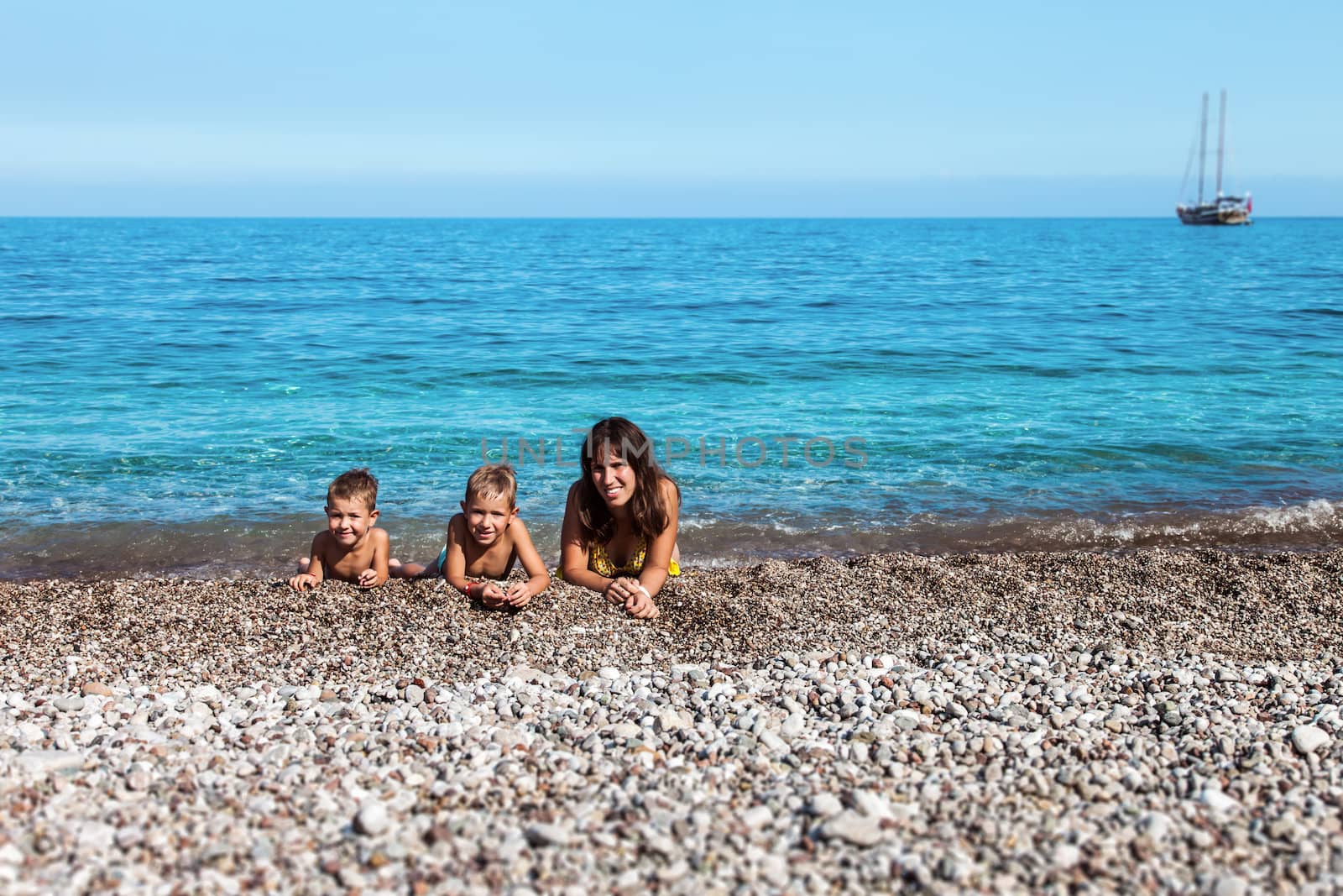 Summer vacations - happy mother with two little smiling child boy brothers playing on blue sea sand beach
