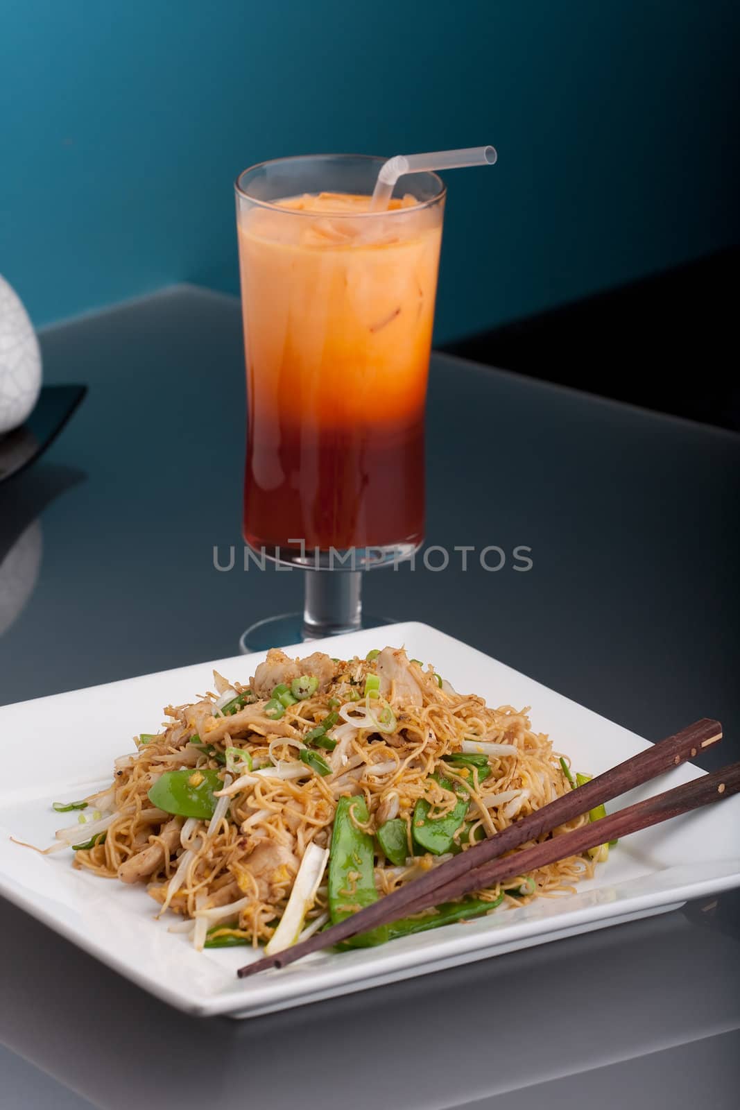 A Thai dish of chicken and noodles stir fry presented on a square white plate with wooden chopsticks.