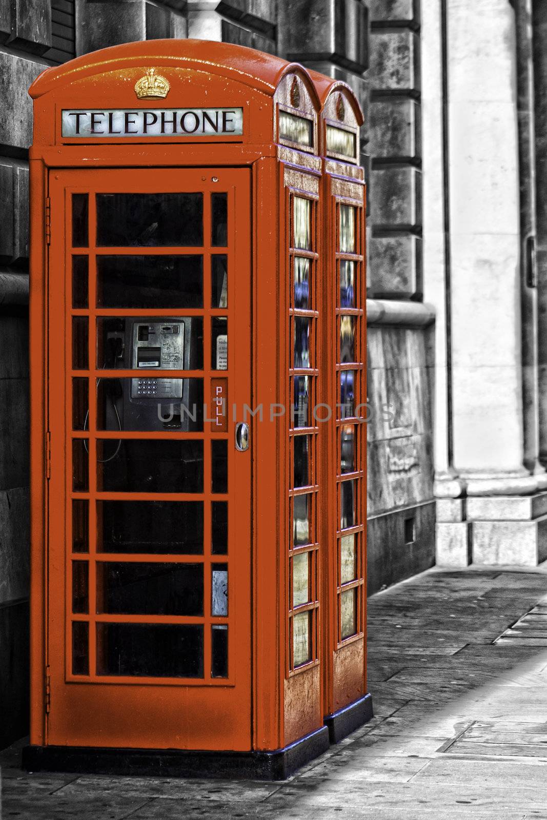 Two iconic red British telephone booths on an urban street with coin-operated payphones for public convenience