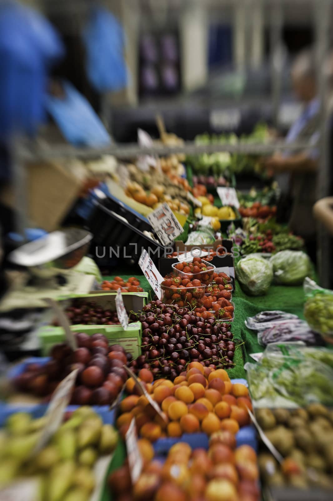 Colourful view down the counter of a stall laden with a variety of fresh fruit and vegetables at a farmers market with selective focus to cherries