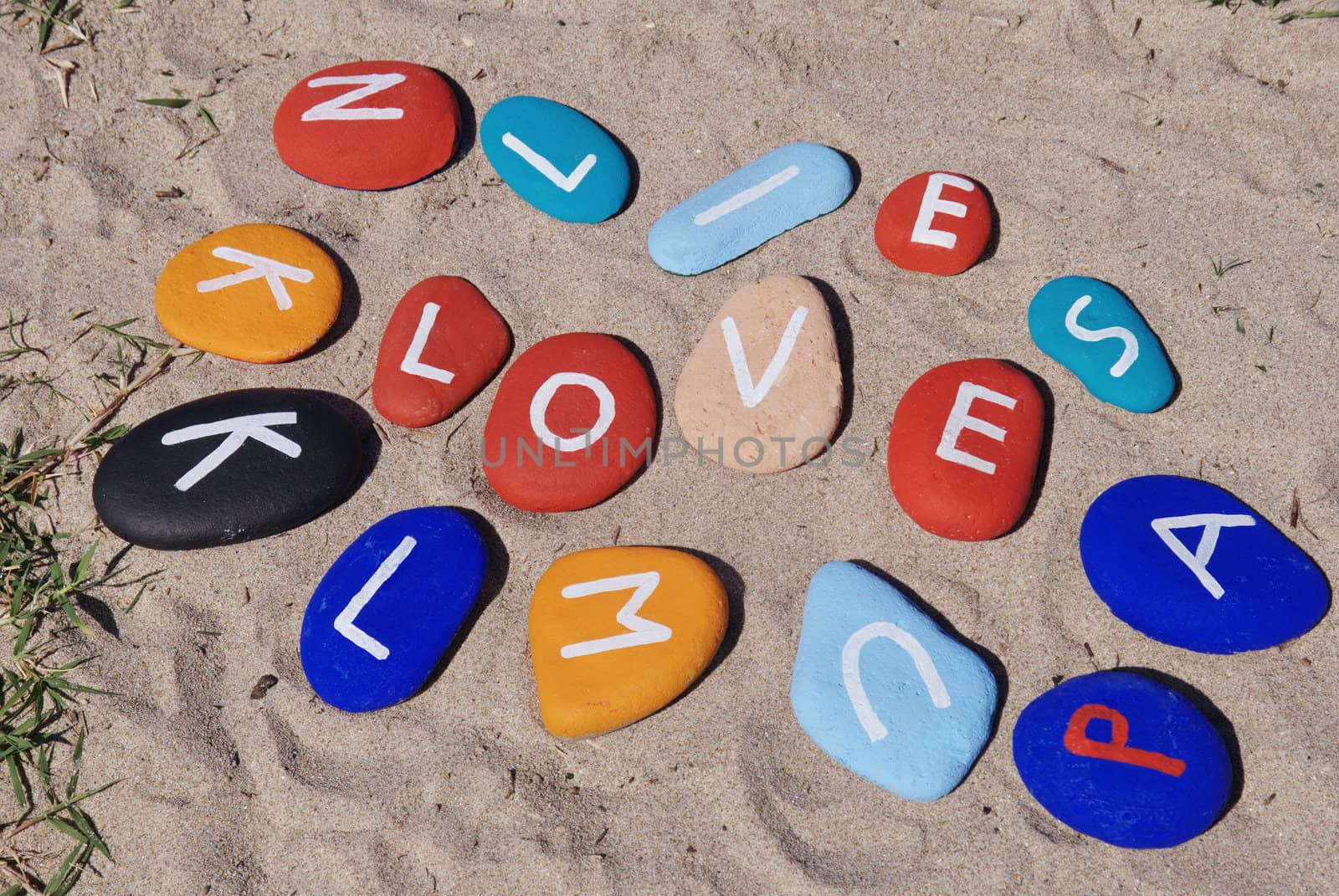 Conceptual stone game of love among colourful stones with sand background