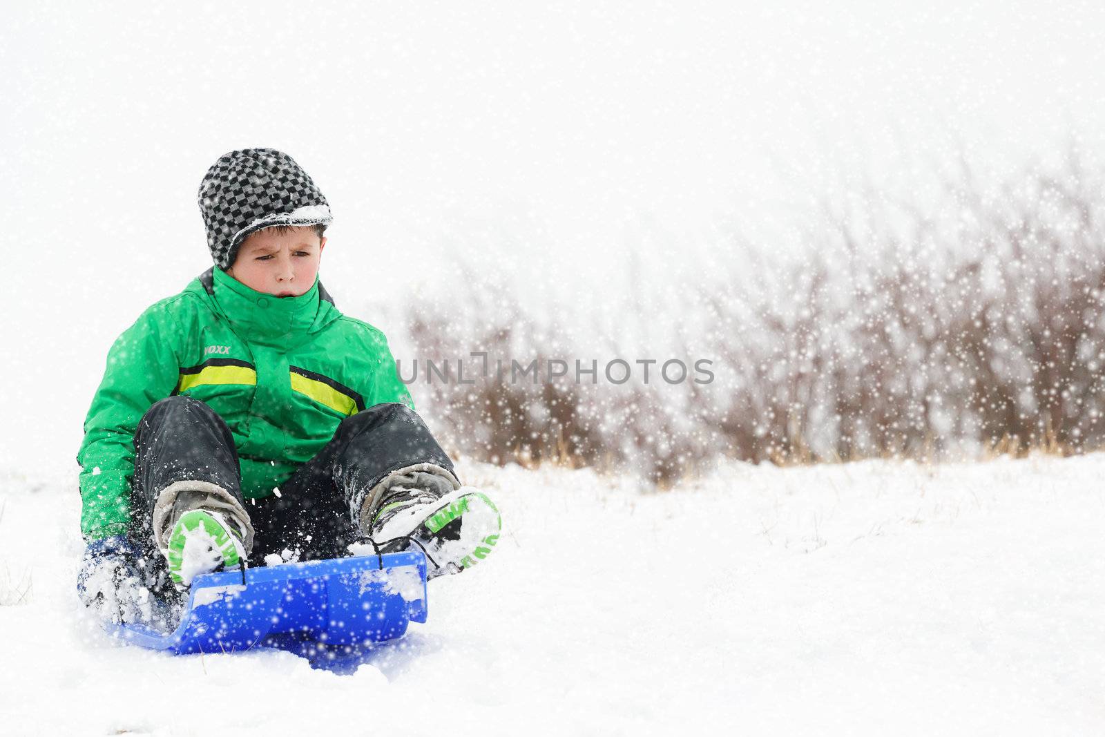 A young boy shows his excitement sledding down a hill in winter