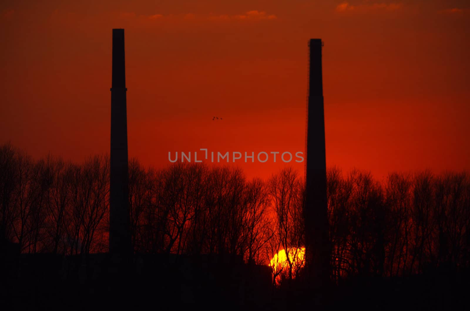 Silhuette of two chimneys in front of a red sunset.