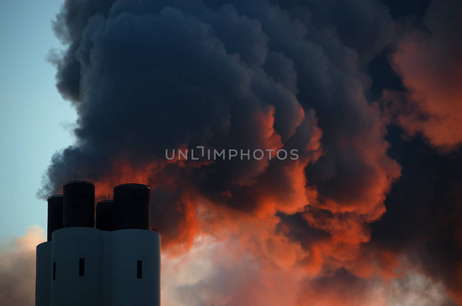 Pollution concept of smoking chimney. The setting sun illuminates the vapor from below, giving it an ominous impression, like that of volcano smoke.