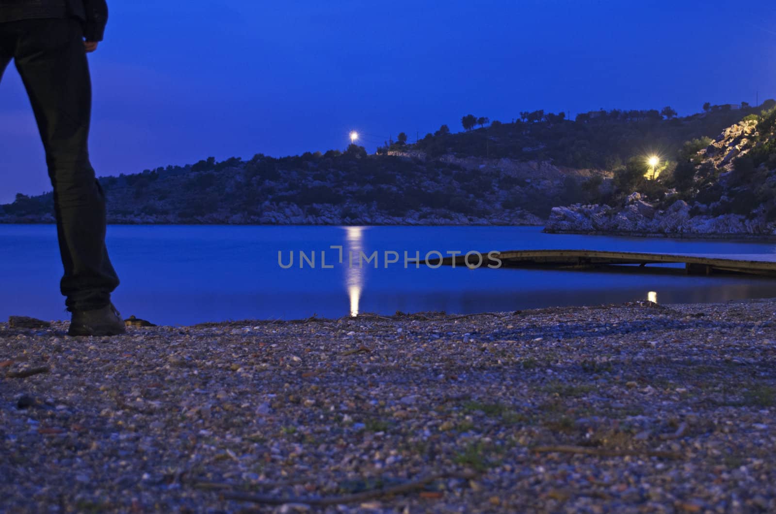 A man standing on a lonely beach at night on Poros island in greece.